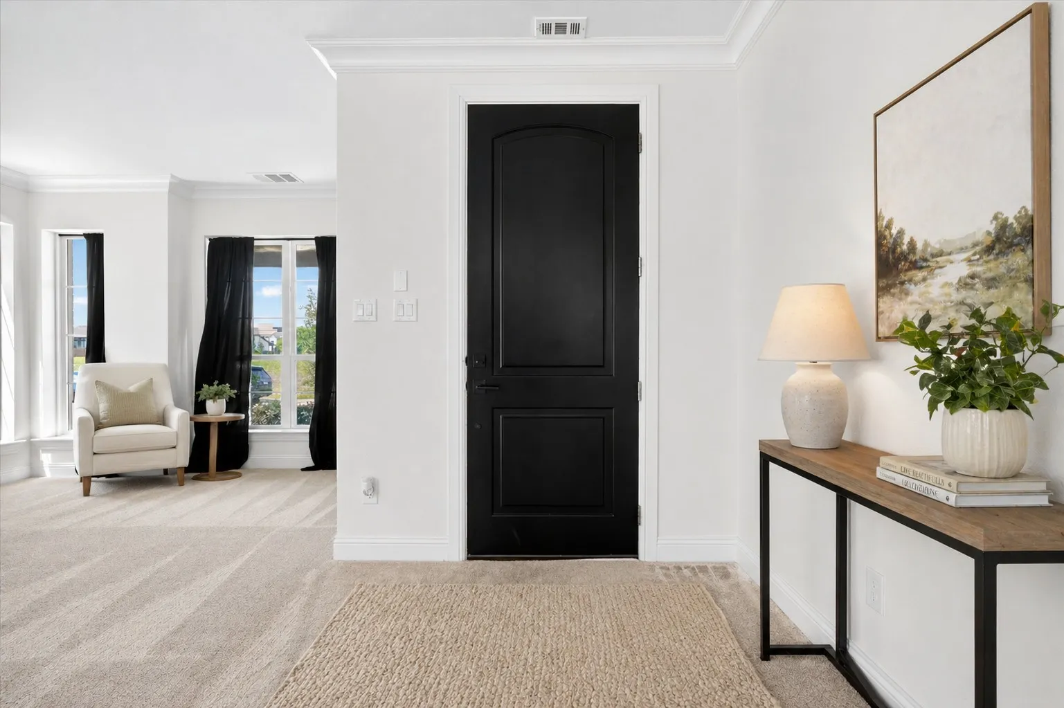 Entryway featuring a contrasting black door with panel detailing, white crown molding, and light -toned carpet flooring Virtually Staged