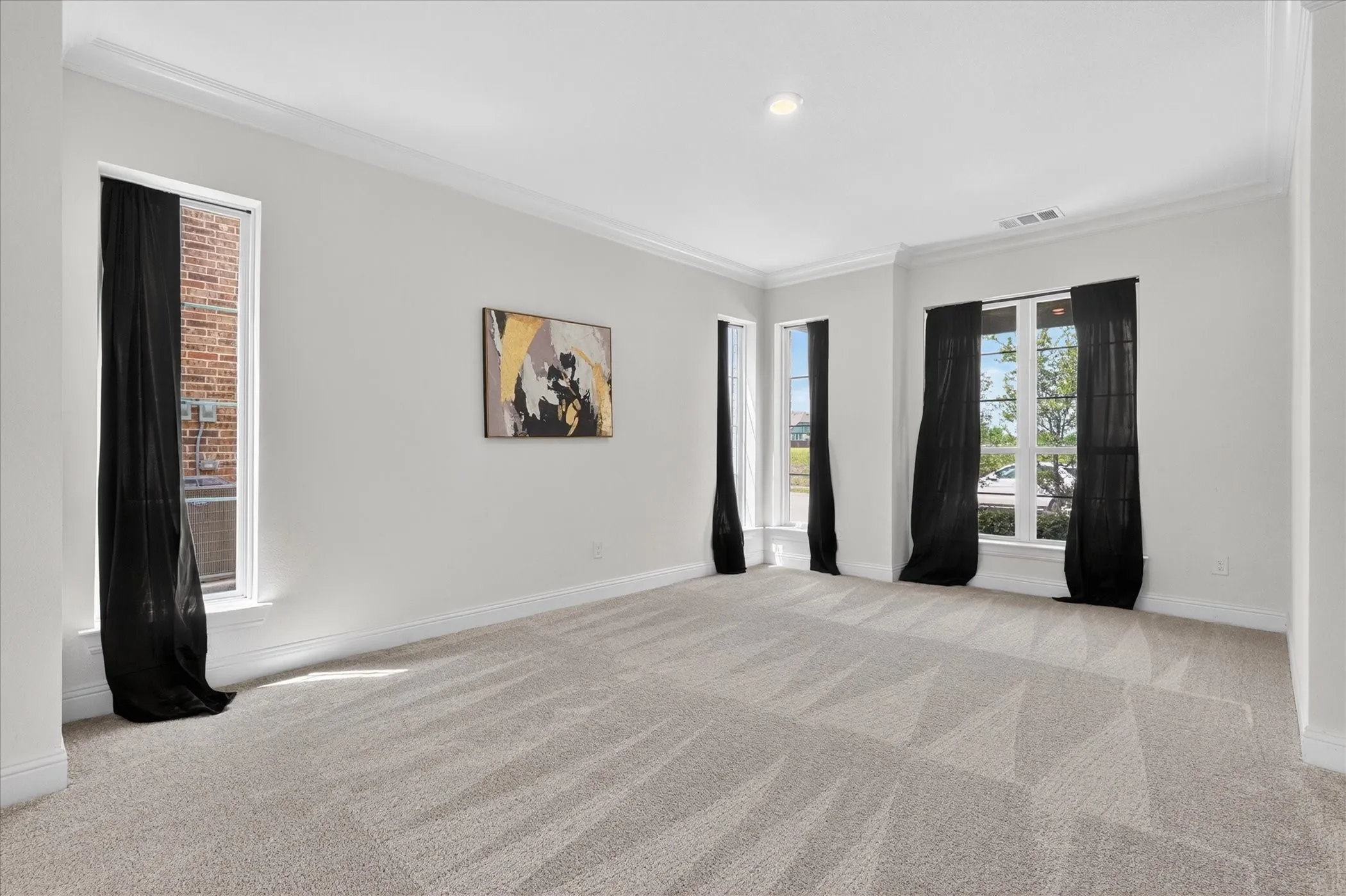 Spacious living area featuring light-toned walls, crown molding, multiple windows with dark drapery, and recessed lighting.