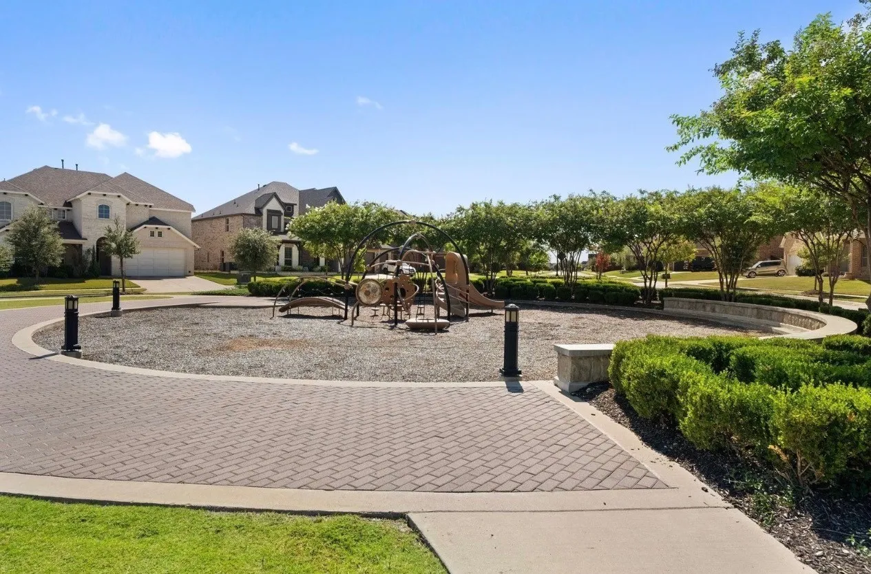 Community park area featuring a playground, paver pathways, and mature landscaping