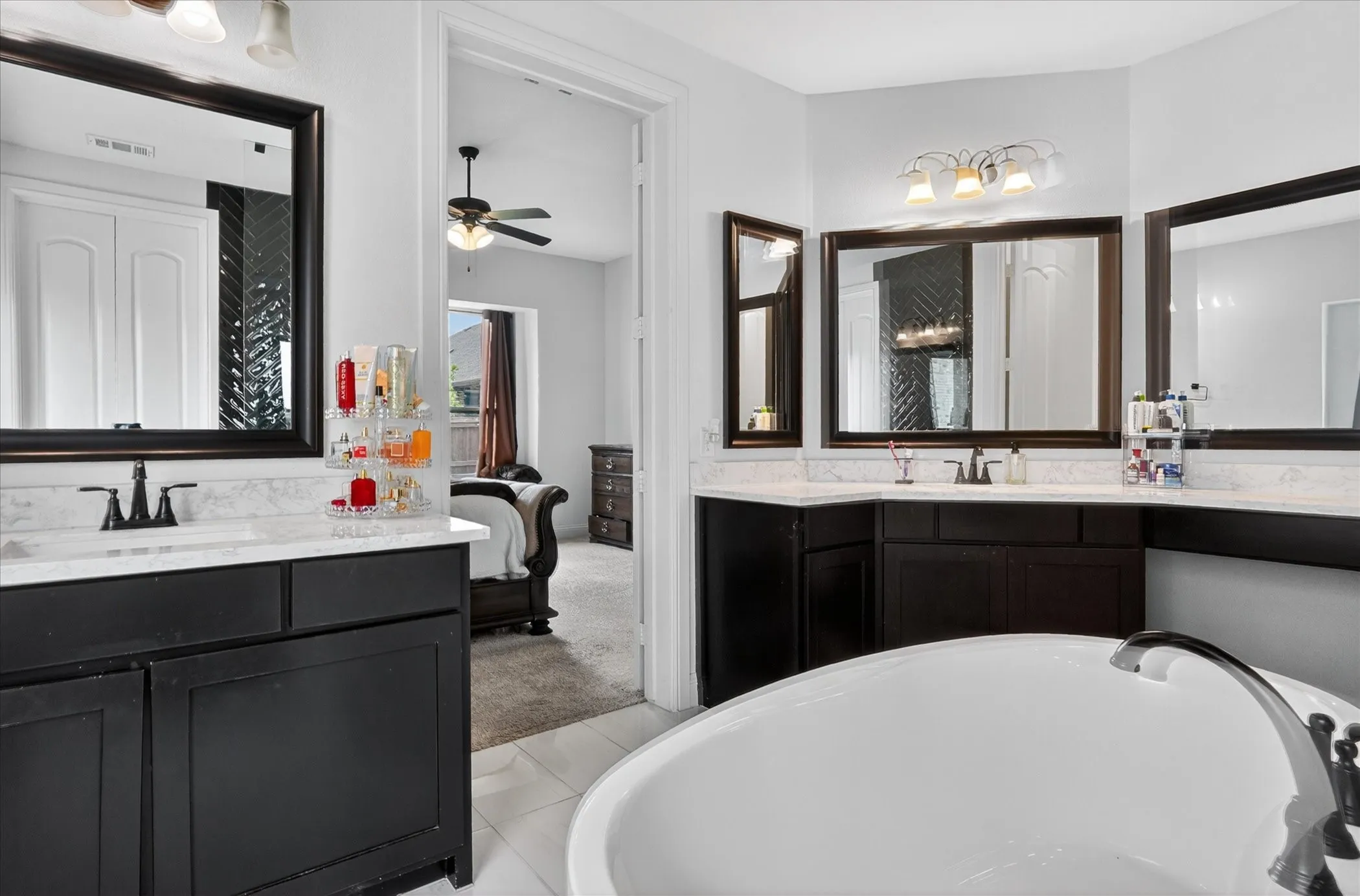 Spacious bathroom featuring a freestanding soaking tub, dual dark wood vanities with undermount sinks, stone countertops, and dark framed mirrors