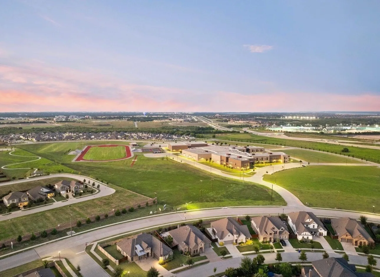 Aerial perspective showcasing a residential development with numerous single-family homes, a contemporary school building, and a multi-lane highway in the distance
