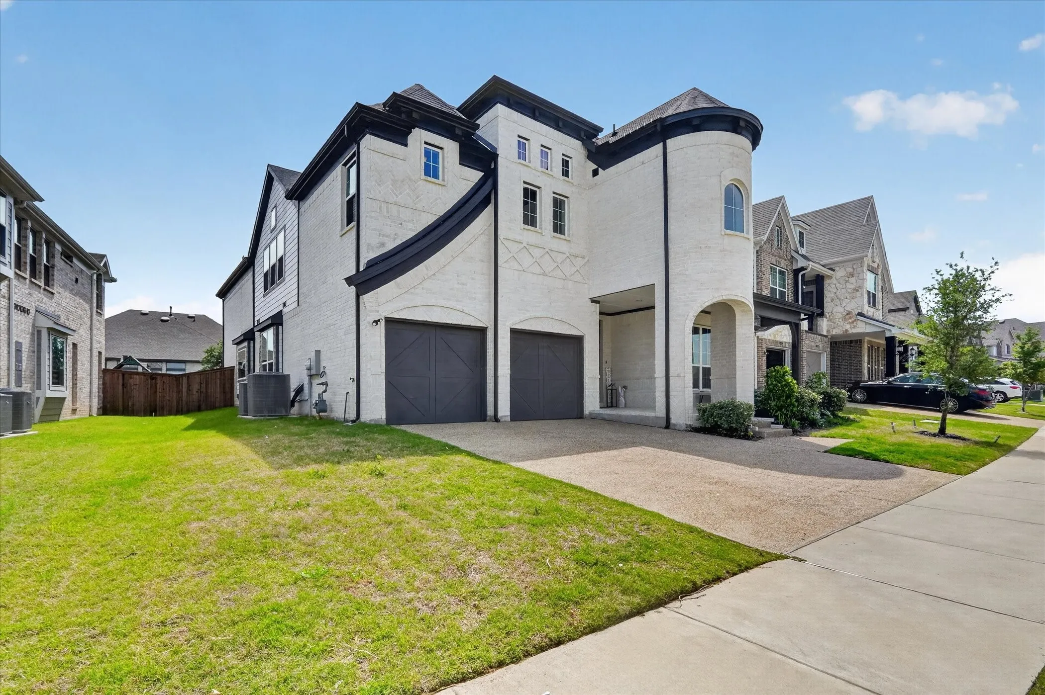 Modern stucco exterior with a prominent turret, dual garage doors, a covered entry, and a gravel style driveway