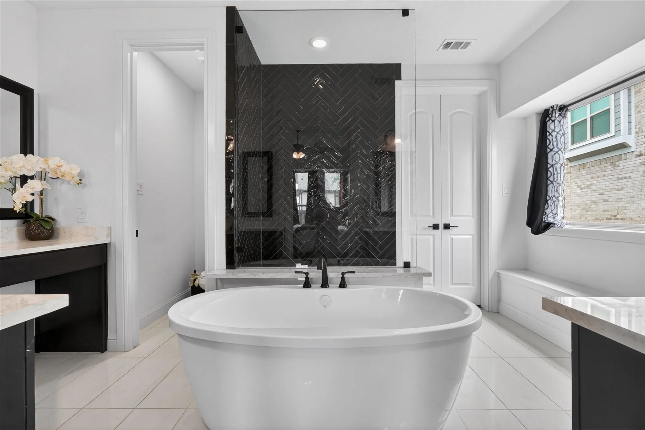 Freestanding soaking tub with matte black fixtures, set against a herringbone-patterned dark tile shower enclosure