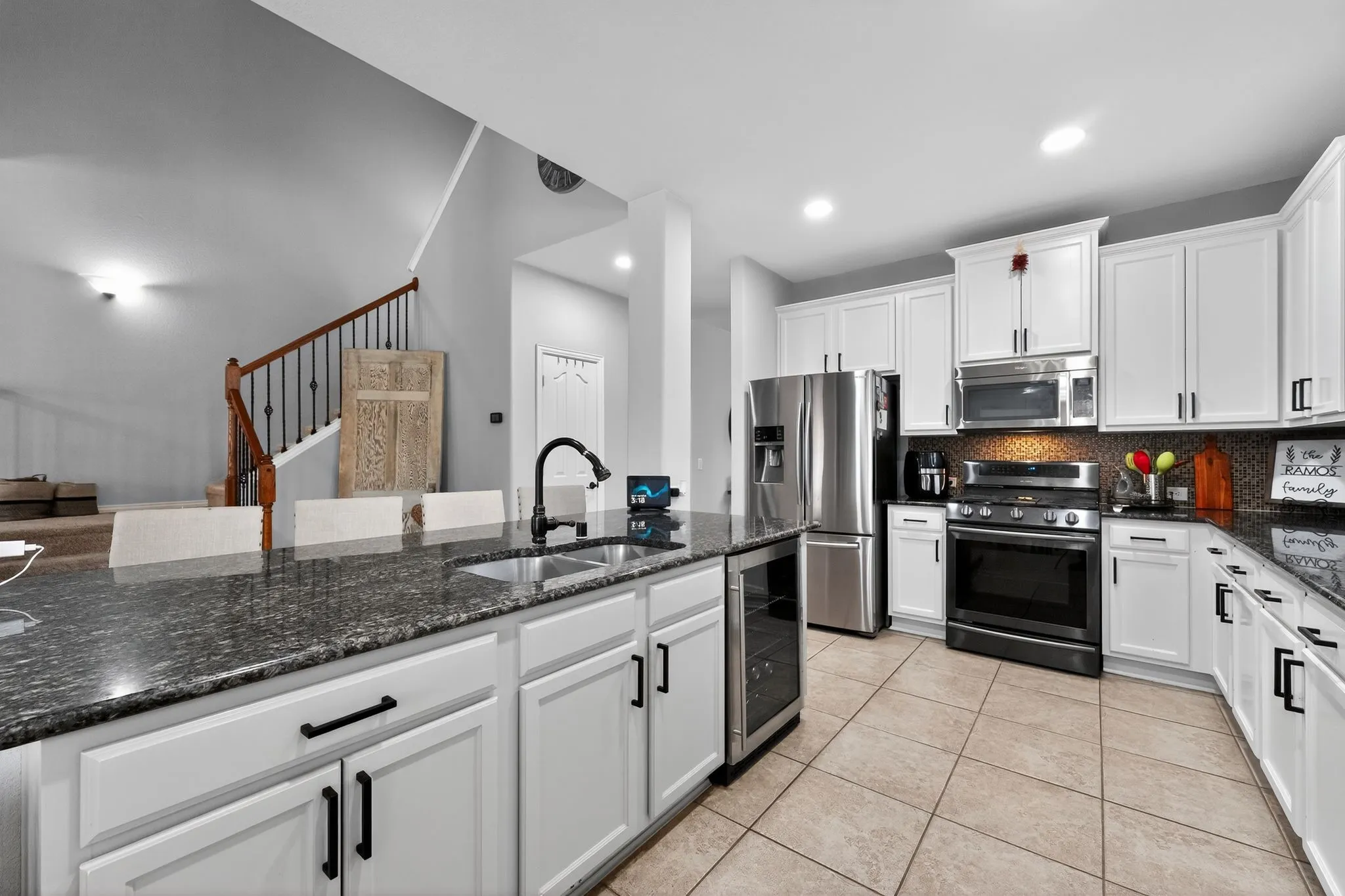 Kitchen featuring white cabinetry with dark hardware, a center island with an undermount sink, dark countertops, stainless steel appliances, and tiled flooring