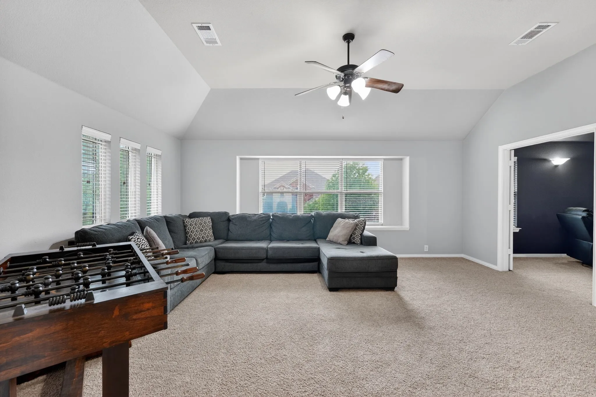 Upstairs spacious room featuring vaulted ceilings, a ceiling fan with light fixture, multiple windows with blinds, and carpet flooring