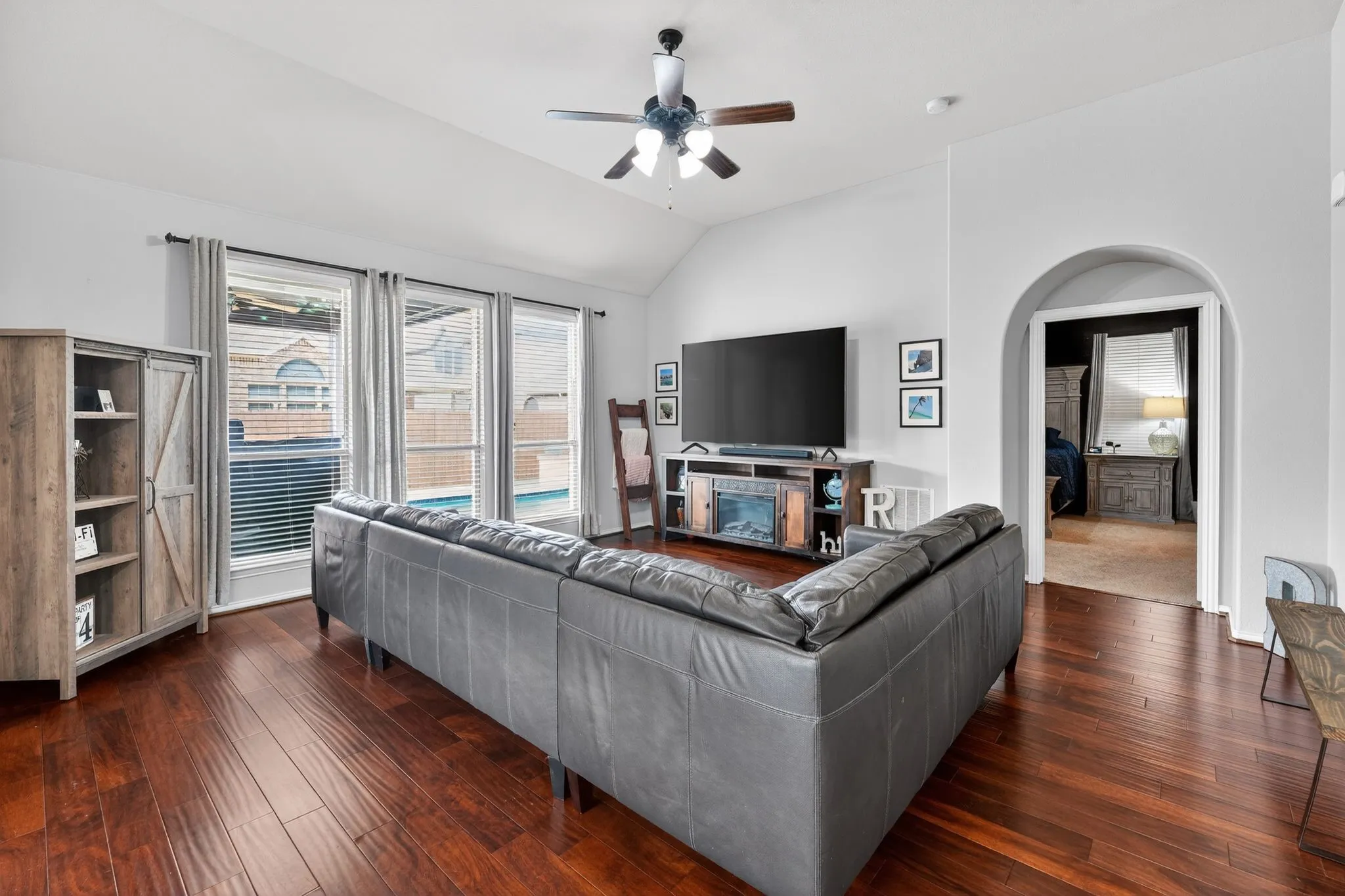 Spacious living area featuring laminate flooring, vaulted ceilings, and a ceiling fan with integrated lighting