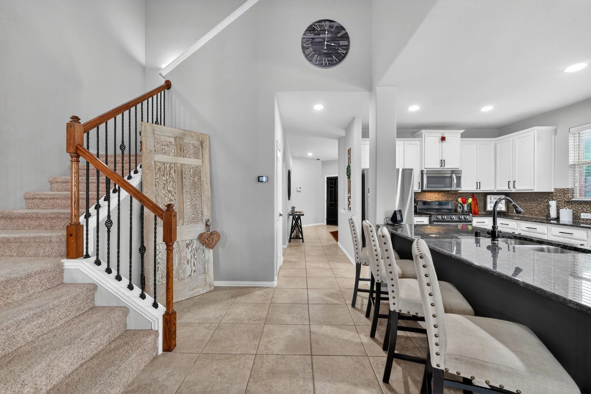 Carpeted staircase with wood handrails and wrought iron balusters, tile flooring, kitchen with granite countertops, white cabinetry, and stainless steel appliances, recessed lighting throughout