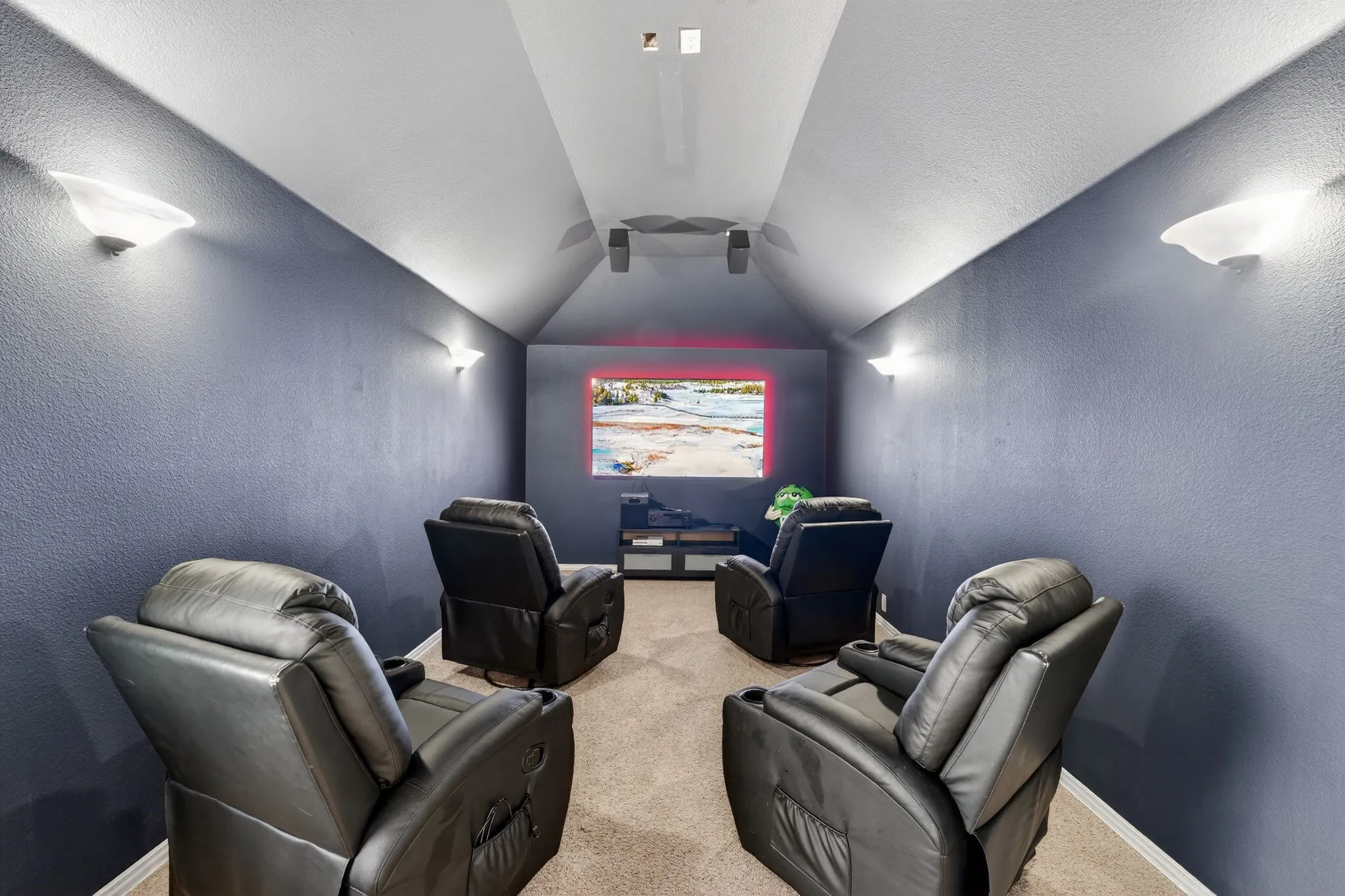 Upstairs - Dedicated media room featuring a large screen, wall-mounted sconce lighting, speakers, and sloped ceilings