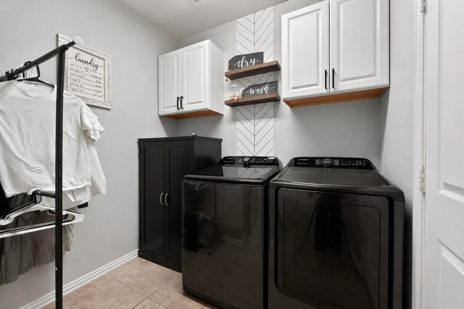 Laundry area featuring white shaker-style cabinetry with dark pulls, wood-finish shelving, and a patterned accent wall