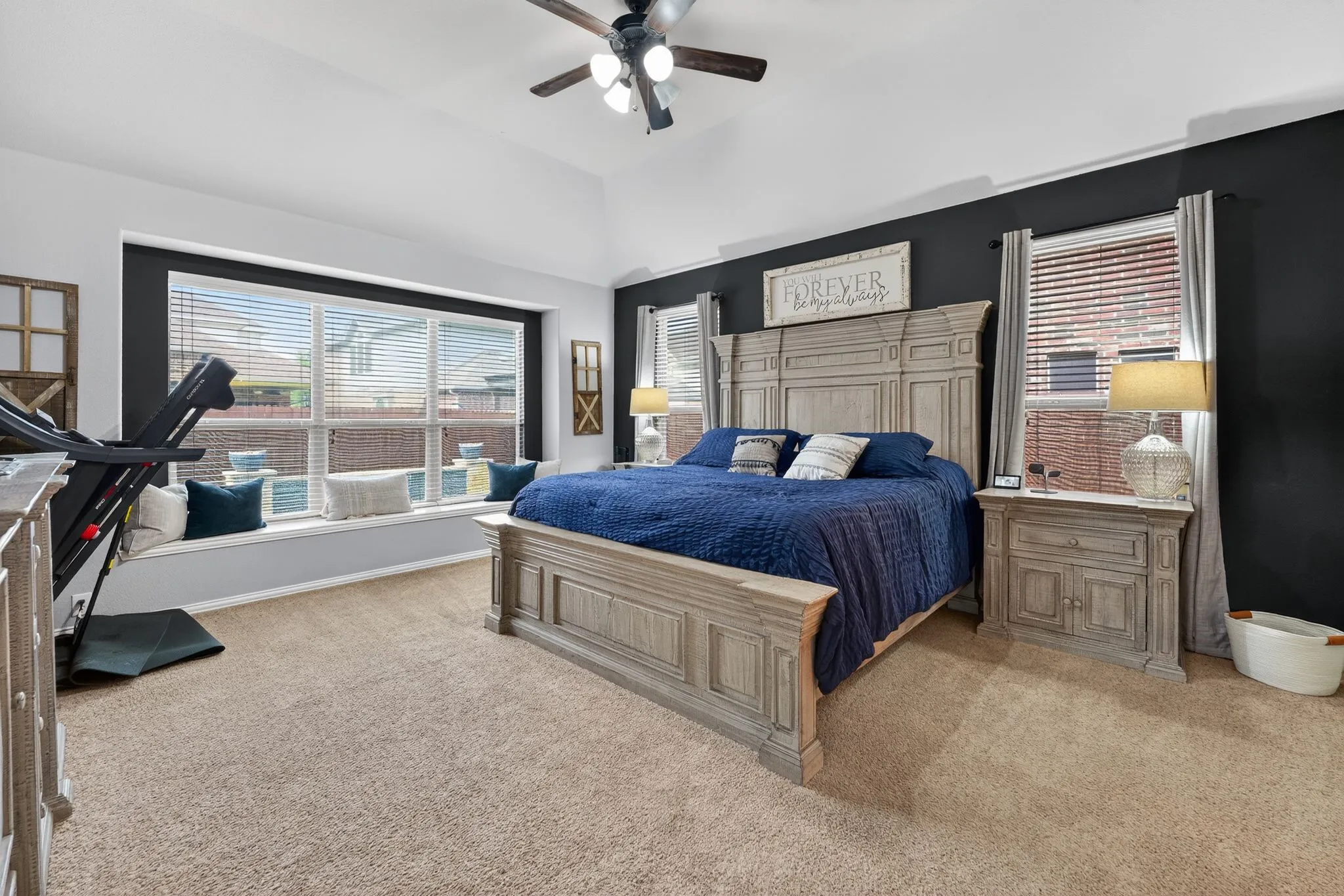 Carpeted bedroom featuring a vaulted ceiling with a ceiling fan, a window seat with ample natural light, and dark accent walls
