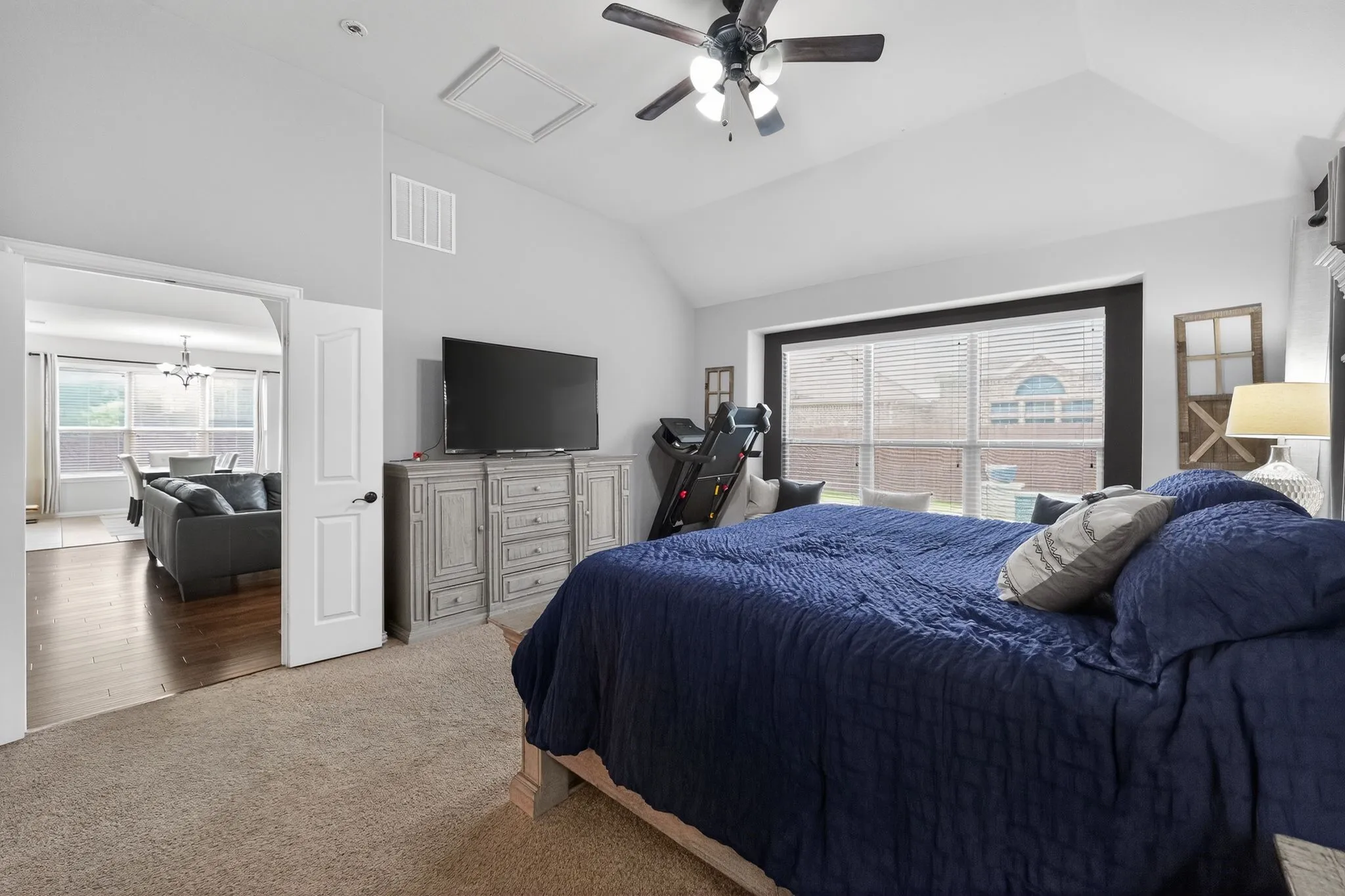 Carpeted bedroom featuring a vaulted ceiling with a ceiling fan, a spacious window with blinds, and a wide entryway