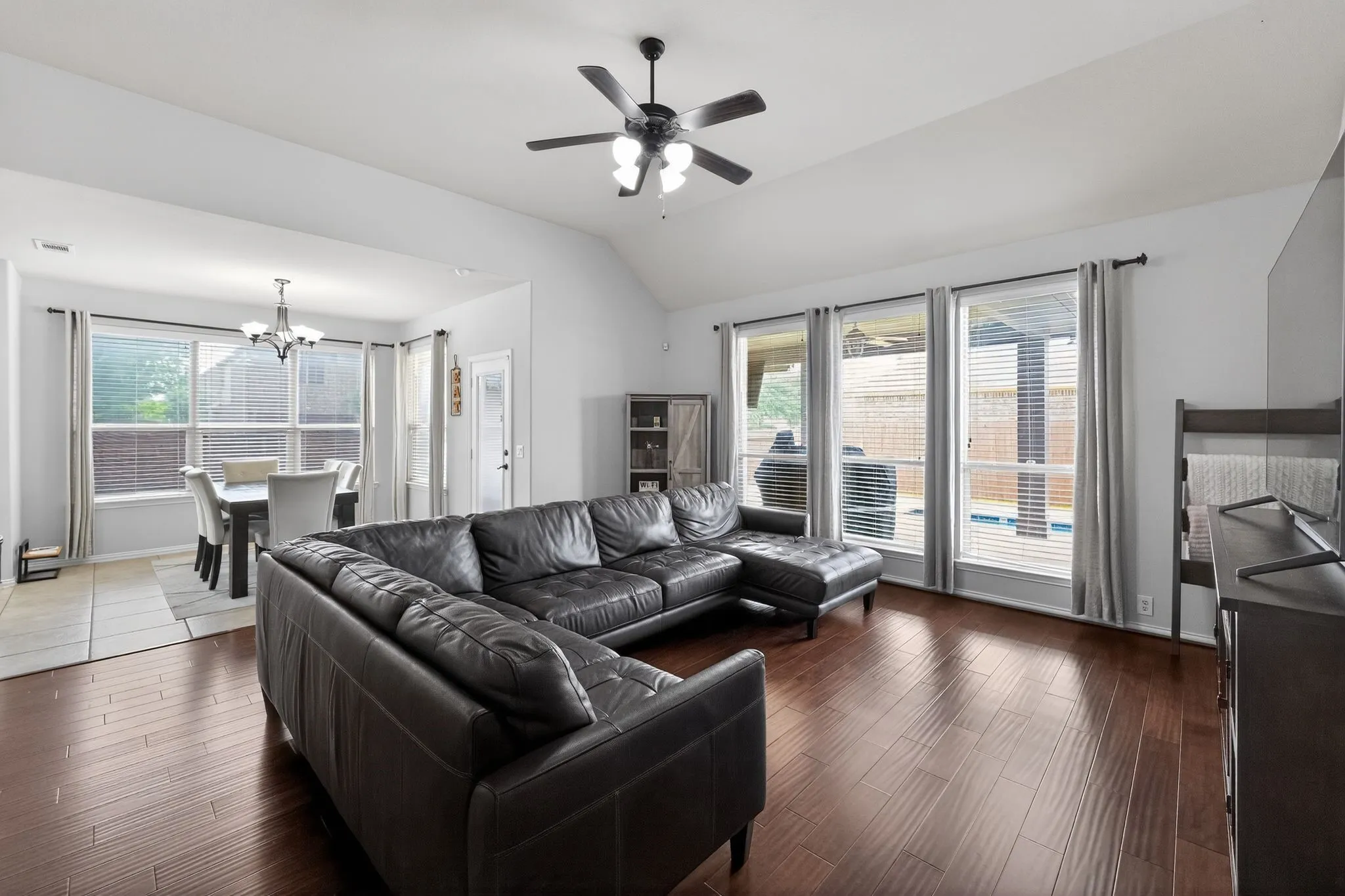 Spacious living area featuring wood-finish flooring, a vaulted ceiling, and an overhead ceiling fan