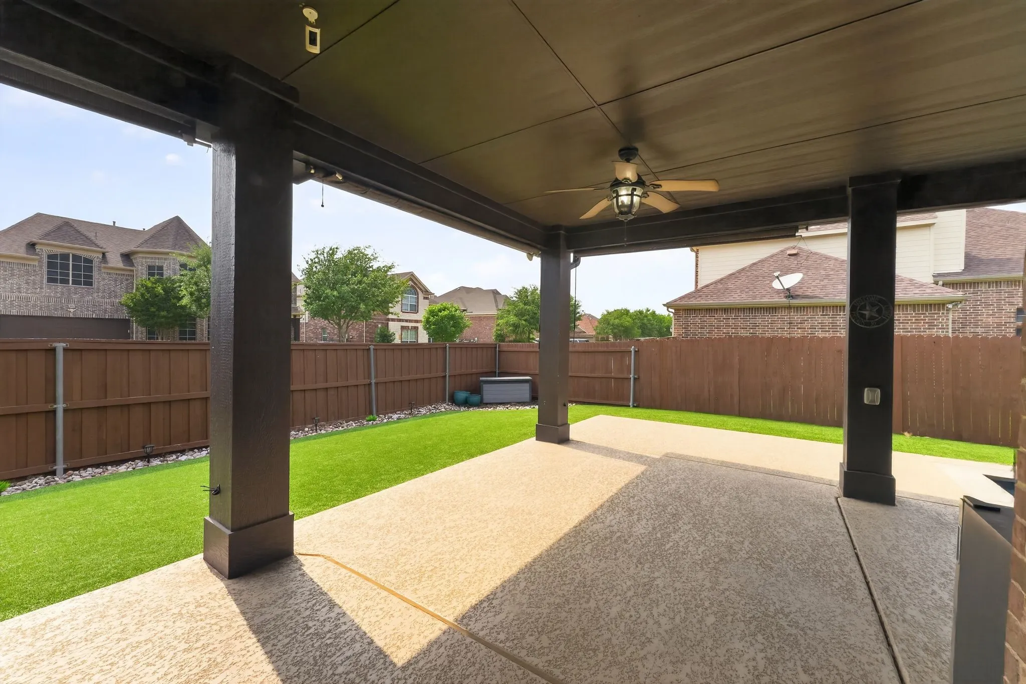 Expansive covered patio featuring a ceiling fan, exposed aggregate concrete flooring, and a flat panel ceiling