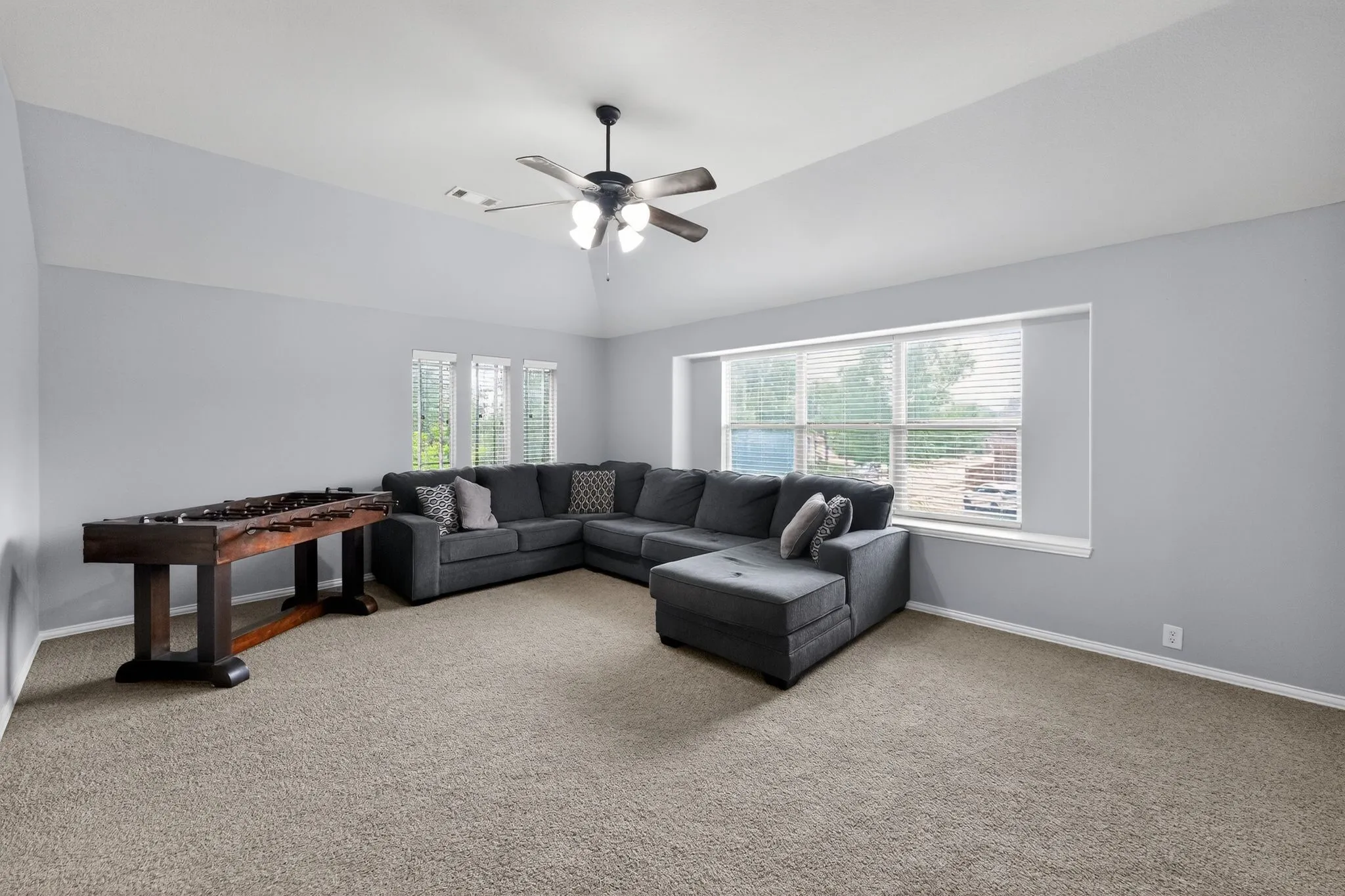 Upstairs spacious entertainment room featuring vaulted ceilings, neutral carpeting, and a ceiling fan with integrated lighting