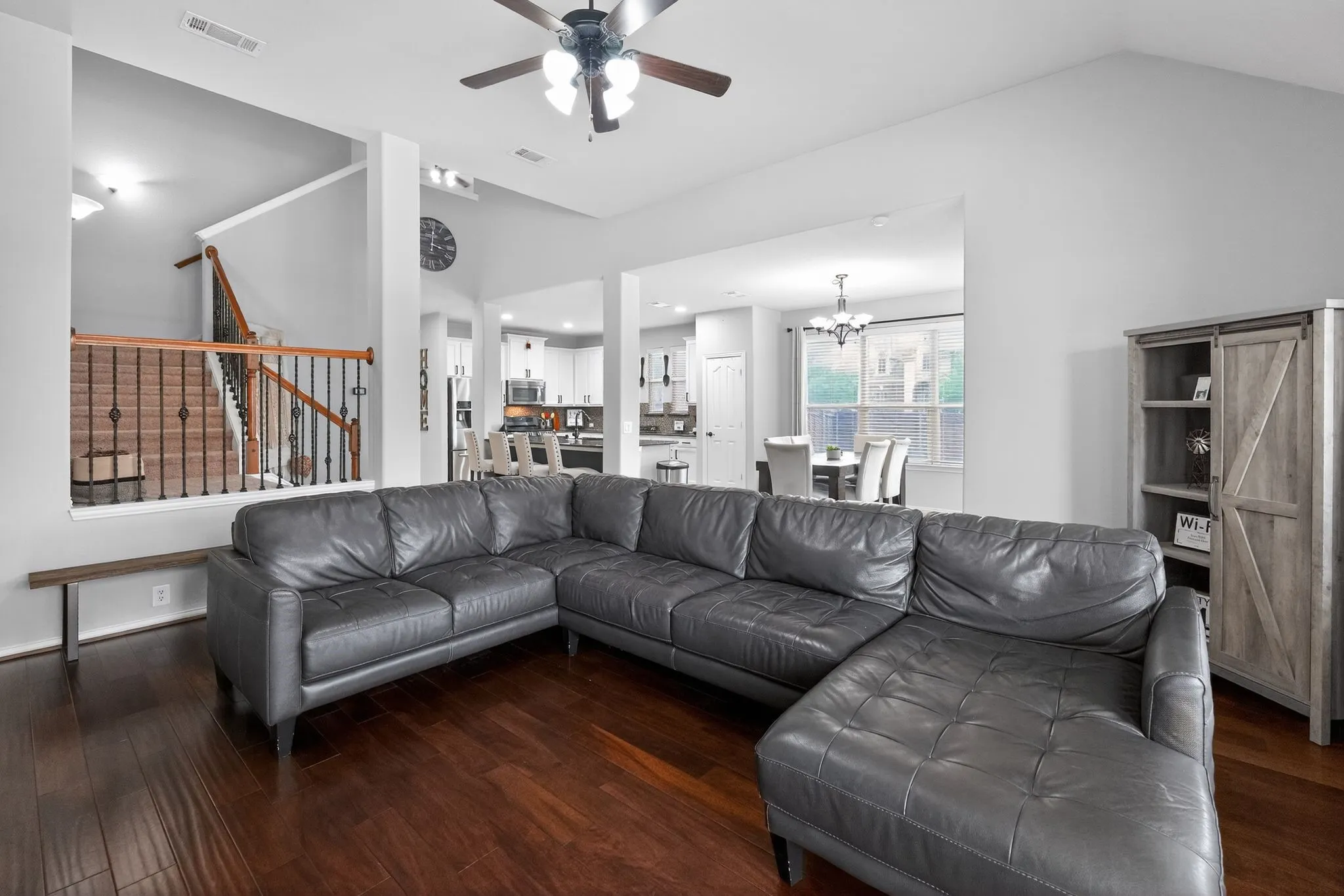 Open-concept living area featuring laminate flooring, a contemporary ceiling fan, and staircase with dark iron balusters