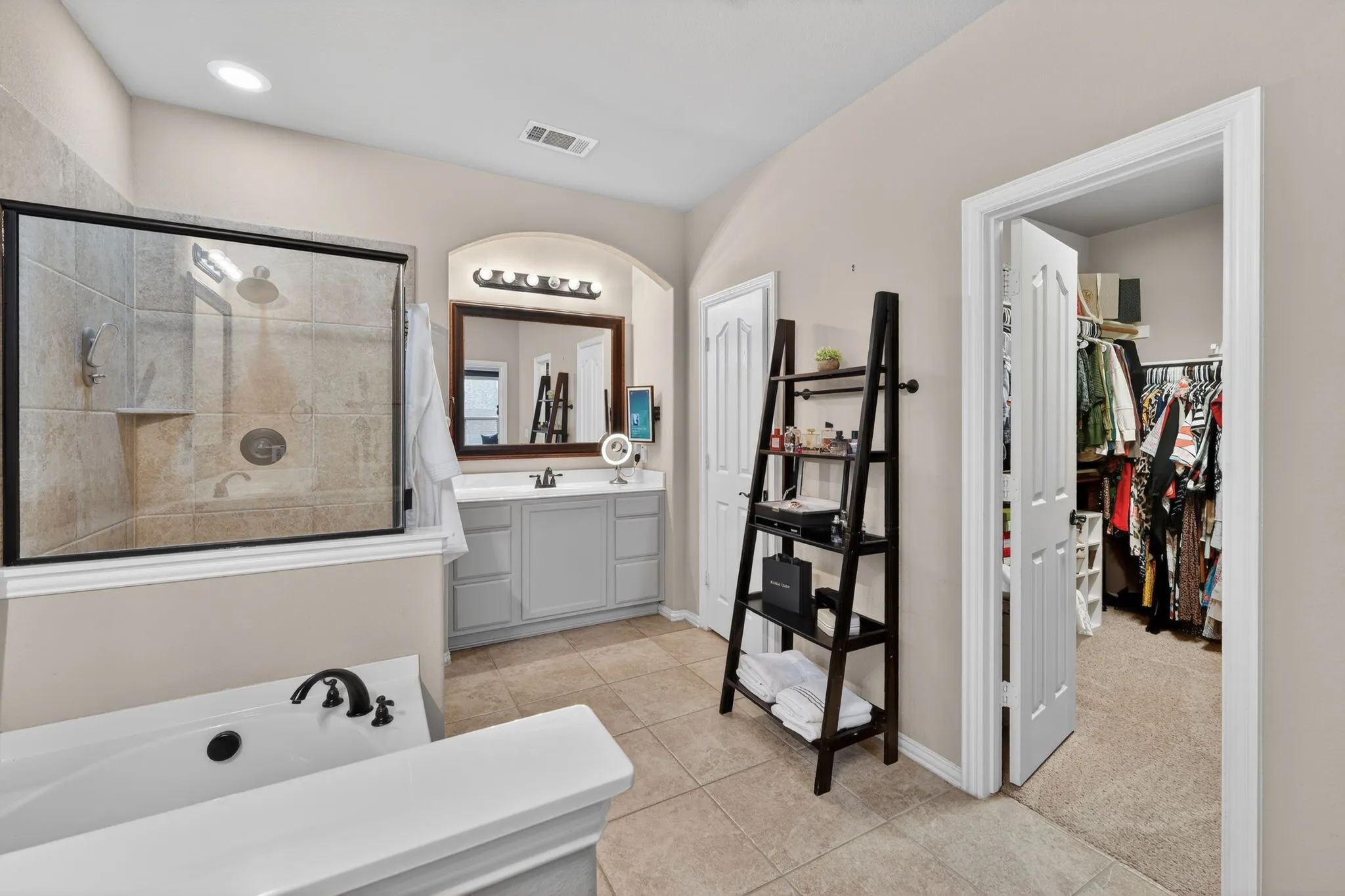 Bathroom featuring a tiled shower with a black frame enclosure, a separate soaking tub with black fixtures, and a vanity with a single sink and wall-mounted lighting