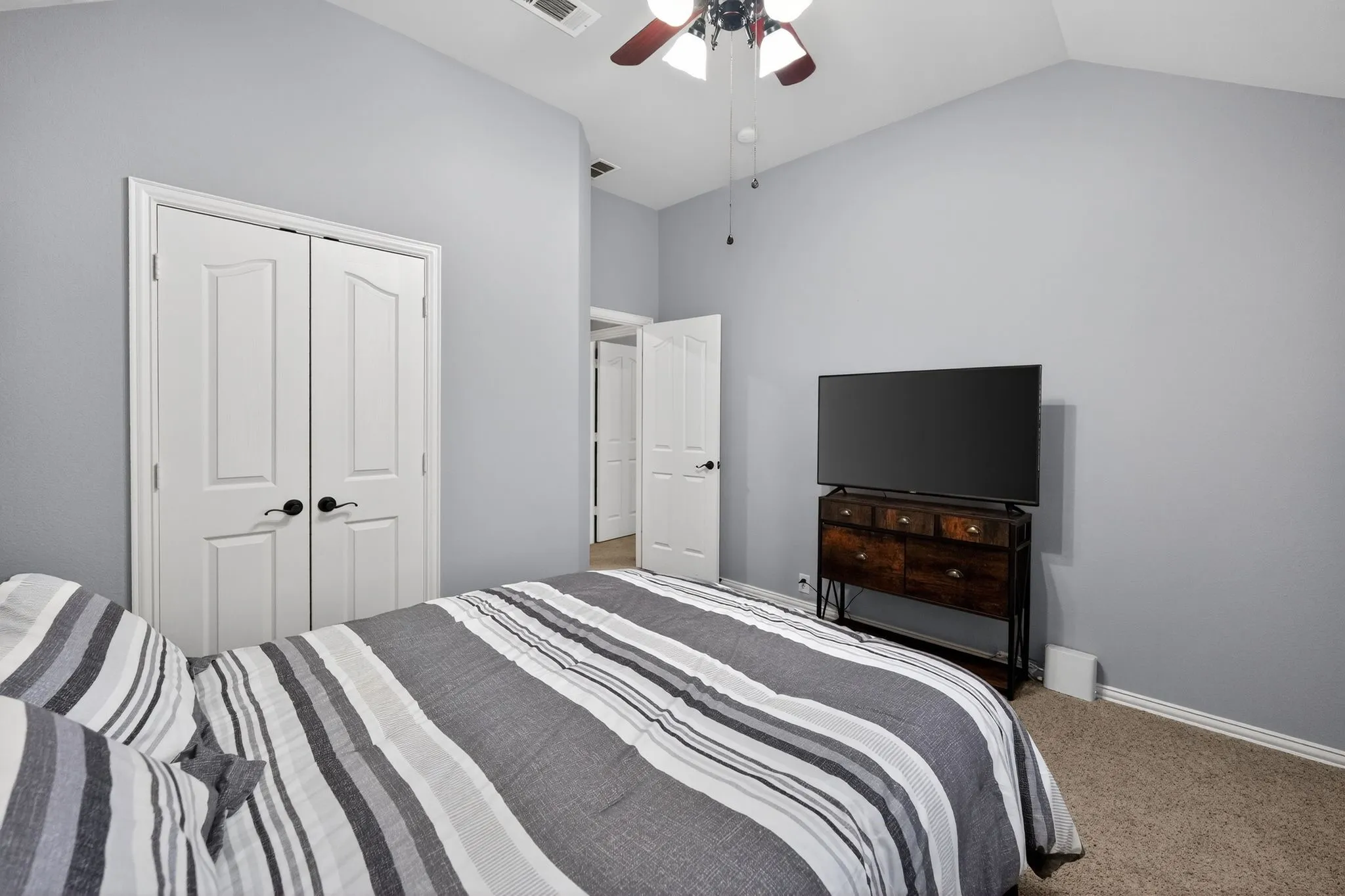 Upstairs - Bedroom # 3 - featuring vaulted ceiling with a ceiling fan, light gray wall paint, white trim, carpet flooring and double door closet