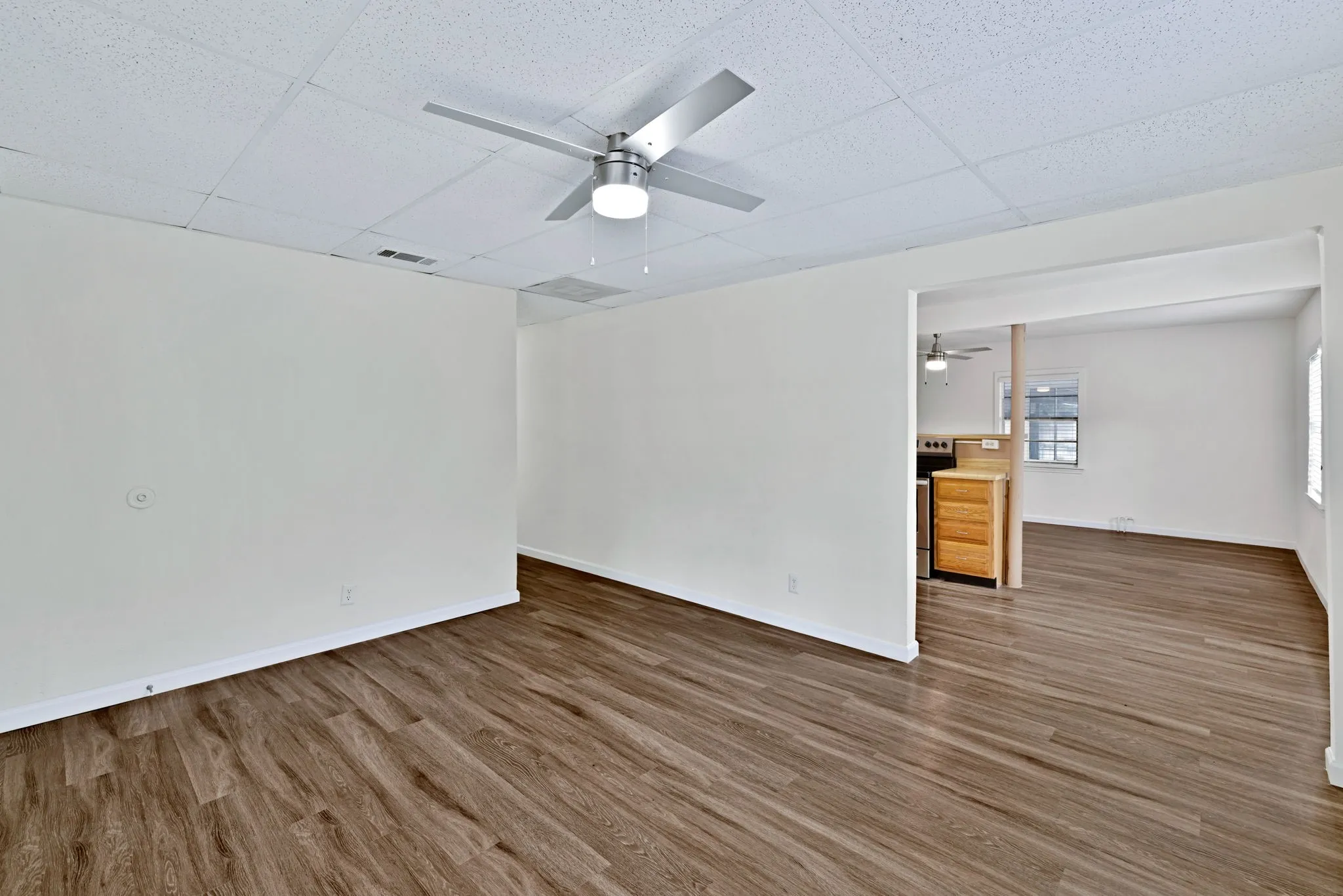 Spacious interior room featuring wood-finish flooring, white walls, and a ceiling fan with integrated lighting