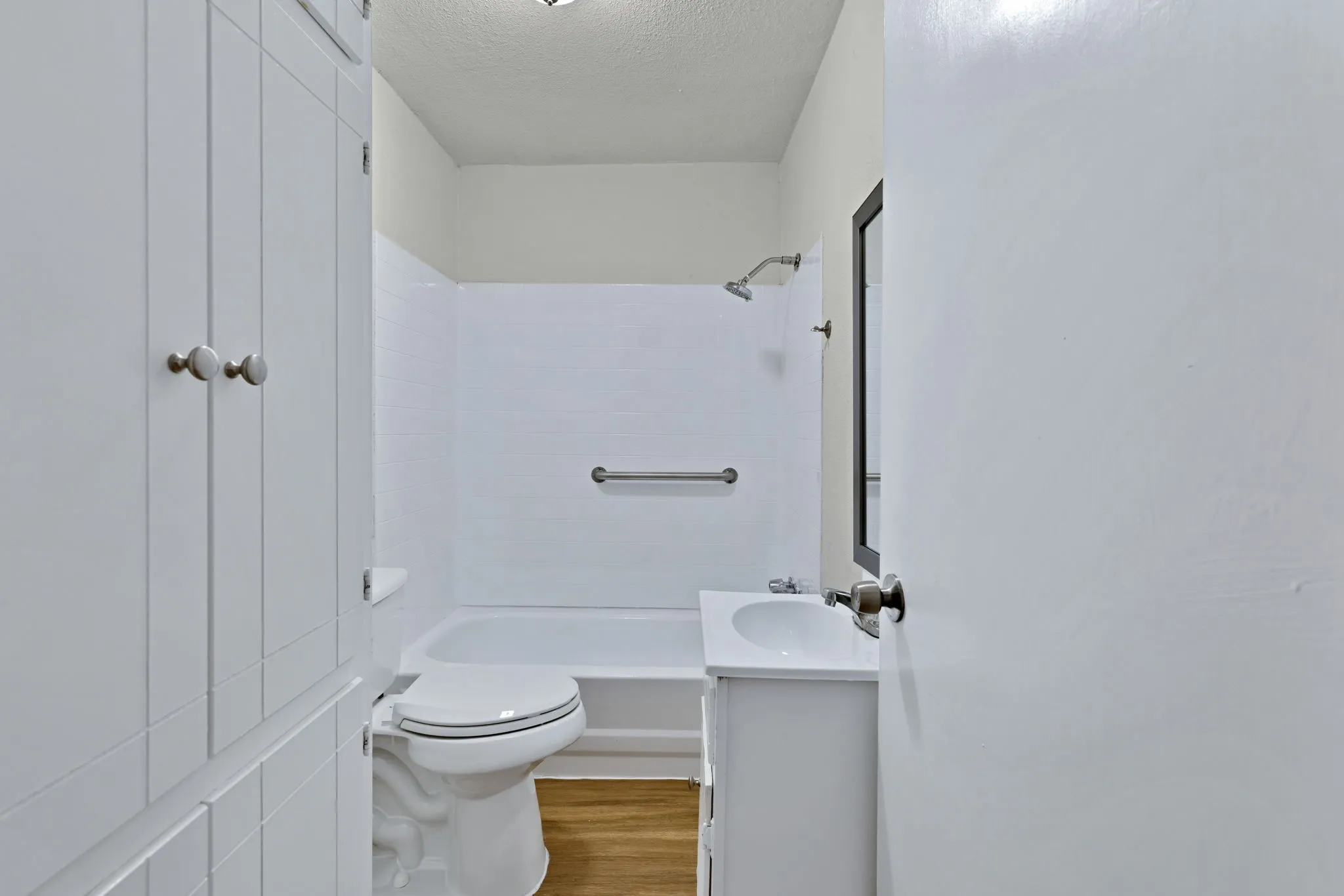 Bathroom featuring a white vanity with integrated sink, a built-in bathtub with shower, a chrome showerhead, and wood-finish flooring