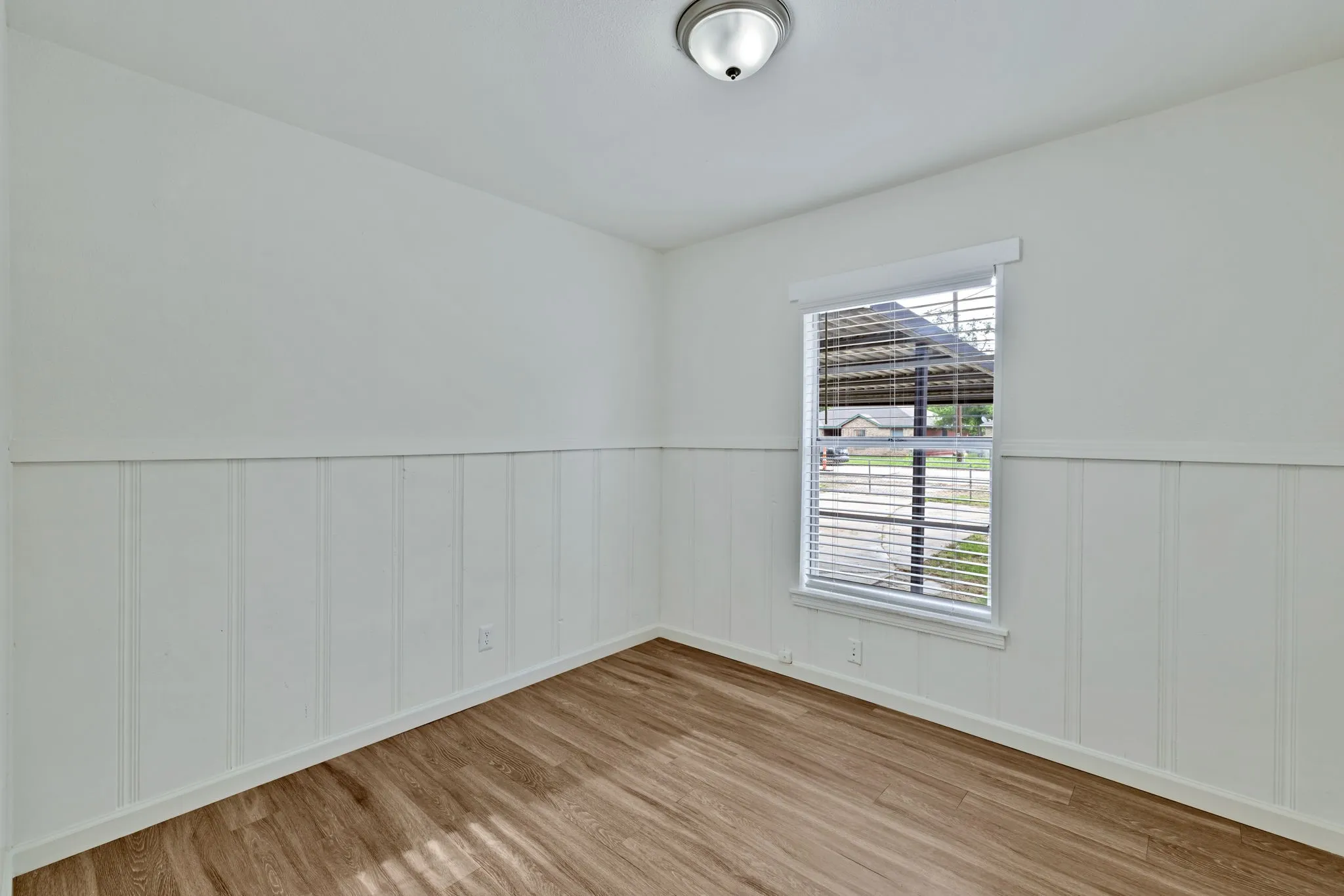 Bright room featuring wood-finish flooring, white wainscoting, and a window with blinds