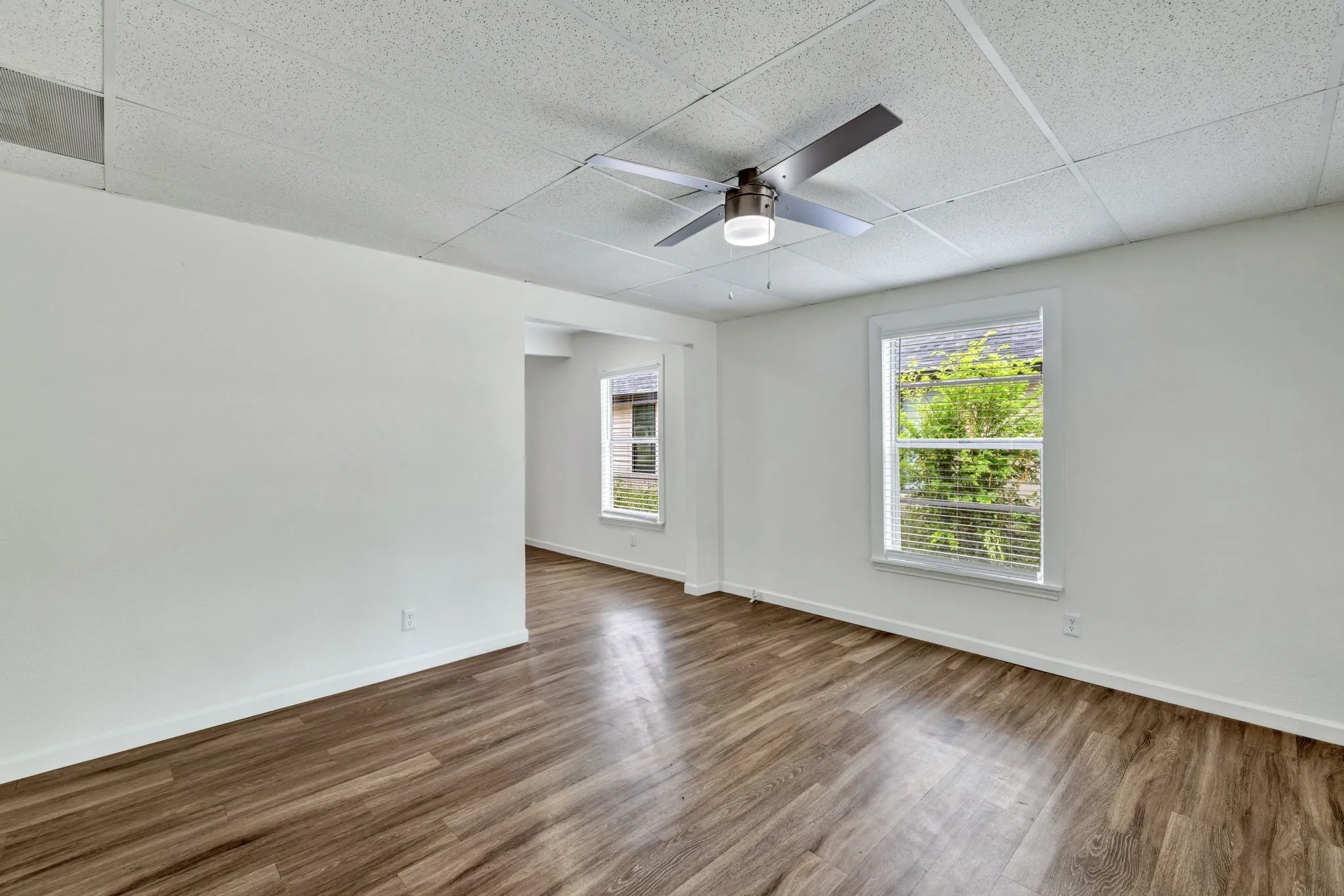 Spacious room featuring wood-finish flooring, crisp white walls, and a contemporary ceiling fan with integrated lighting