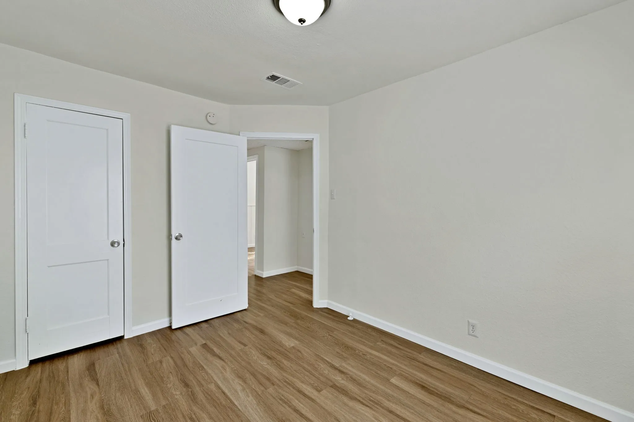 Neutral-toned room featuring light wood-finish flooring, white baseboards, and a flush mount ceiling light