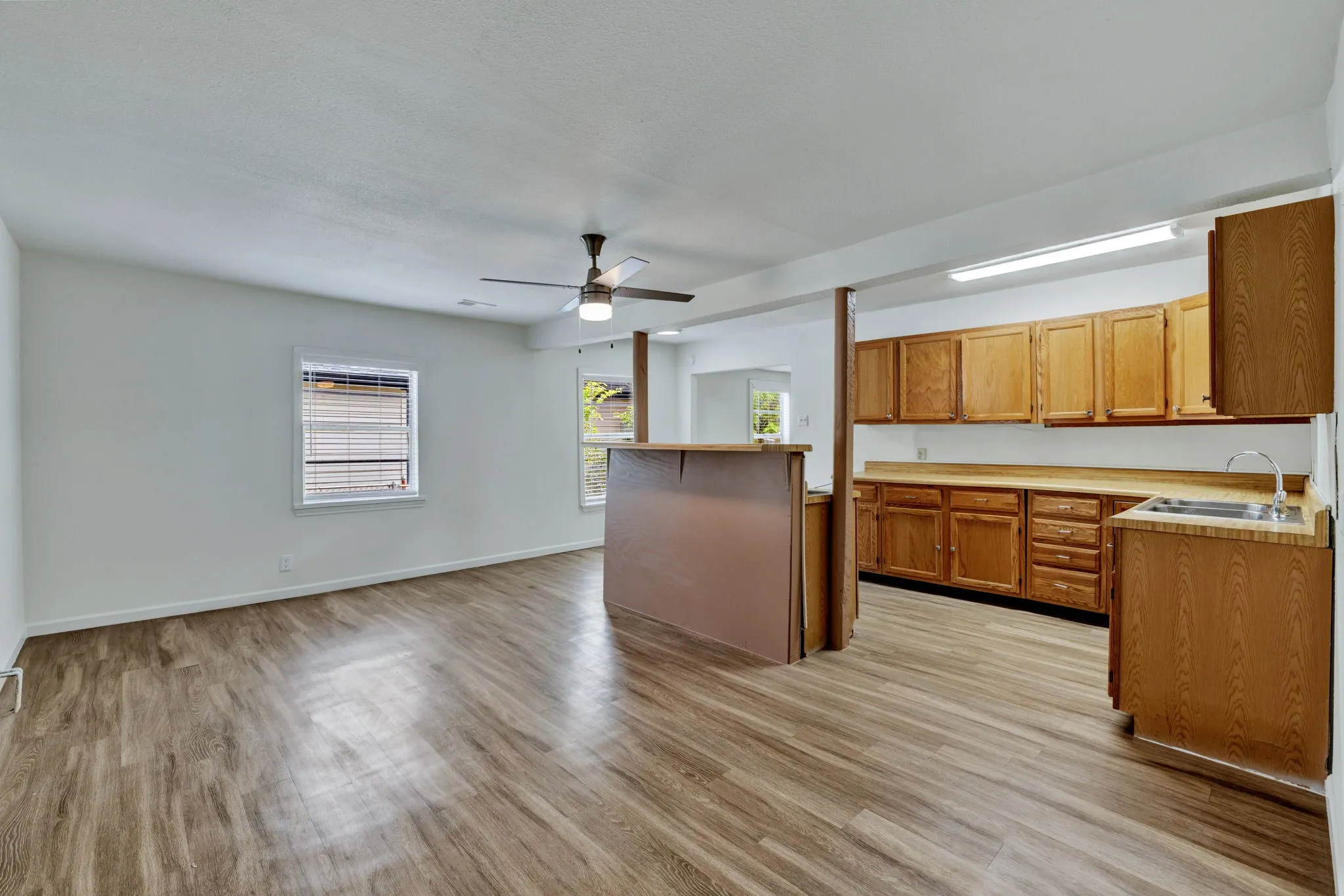 Open-concept living area featuring wood-finish flooring, a ceiling fan with integrated lighting, and white walls