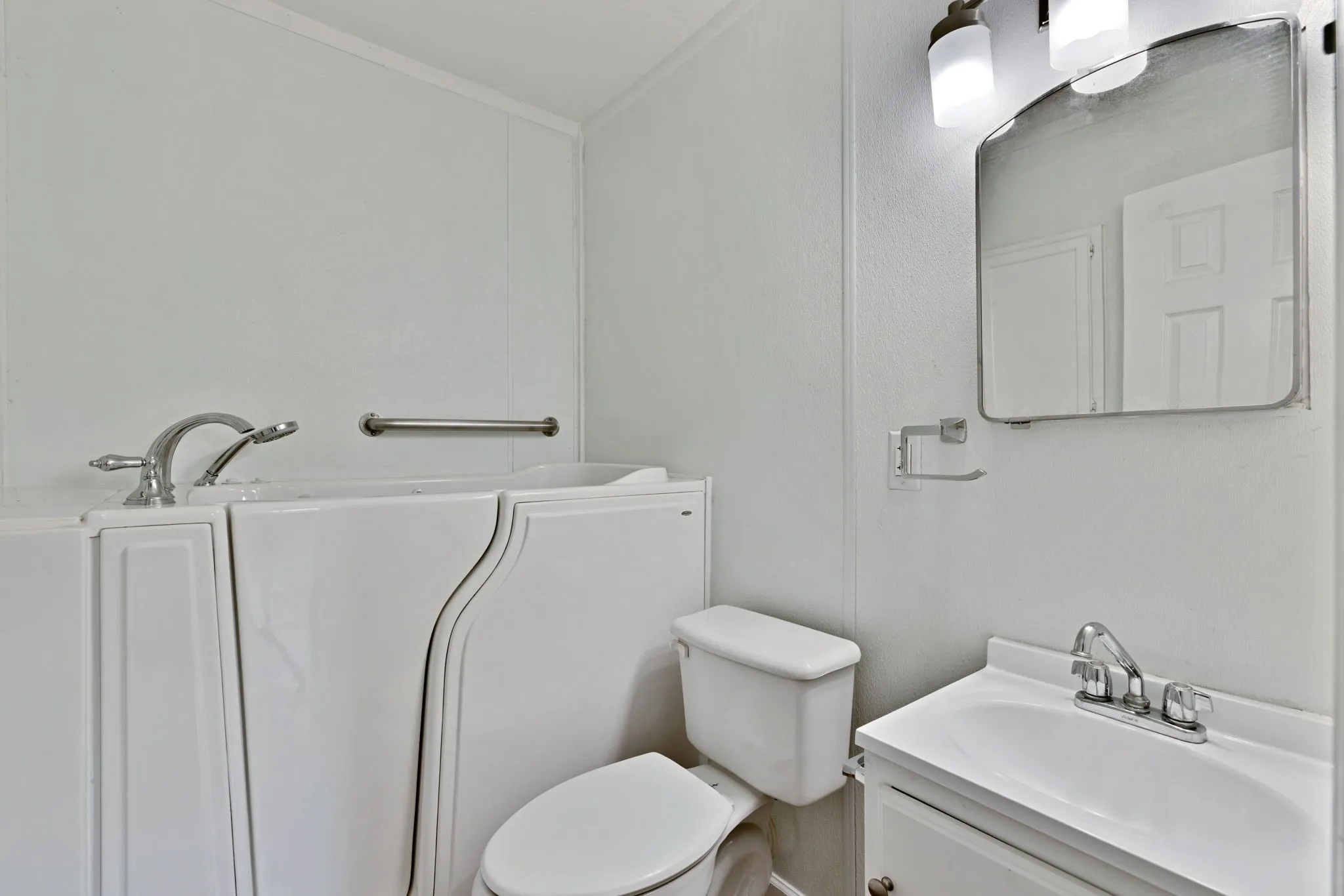 Bathroom featuring a white walk-in bathtub with chrome fixtures, a white toilet, and a vanity with an integrated sink and chrome faucet