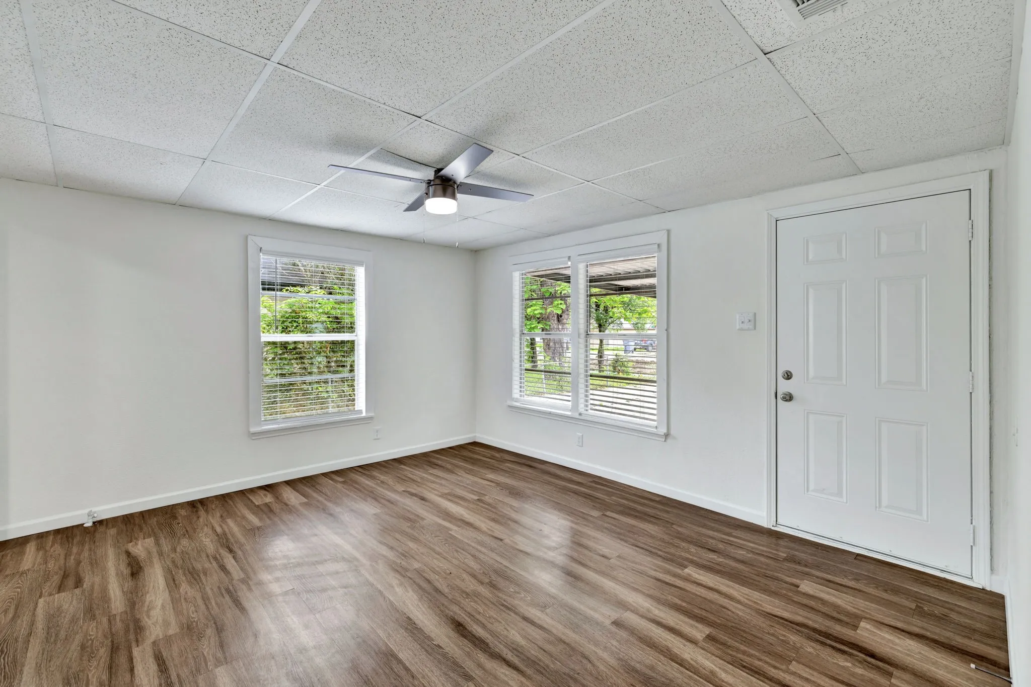Spacious room featuring wood-finish flooring, white walls, and a drop ceiling with integrated lighting
