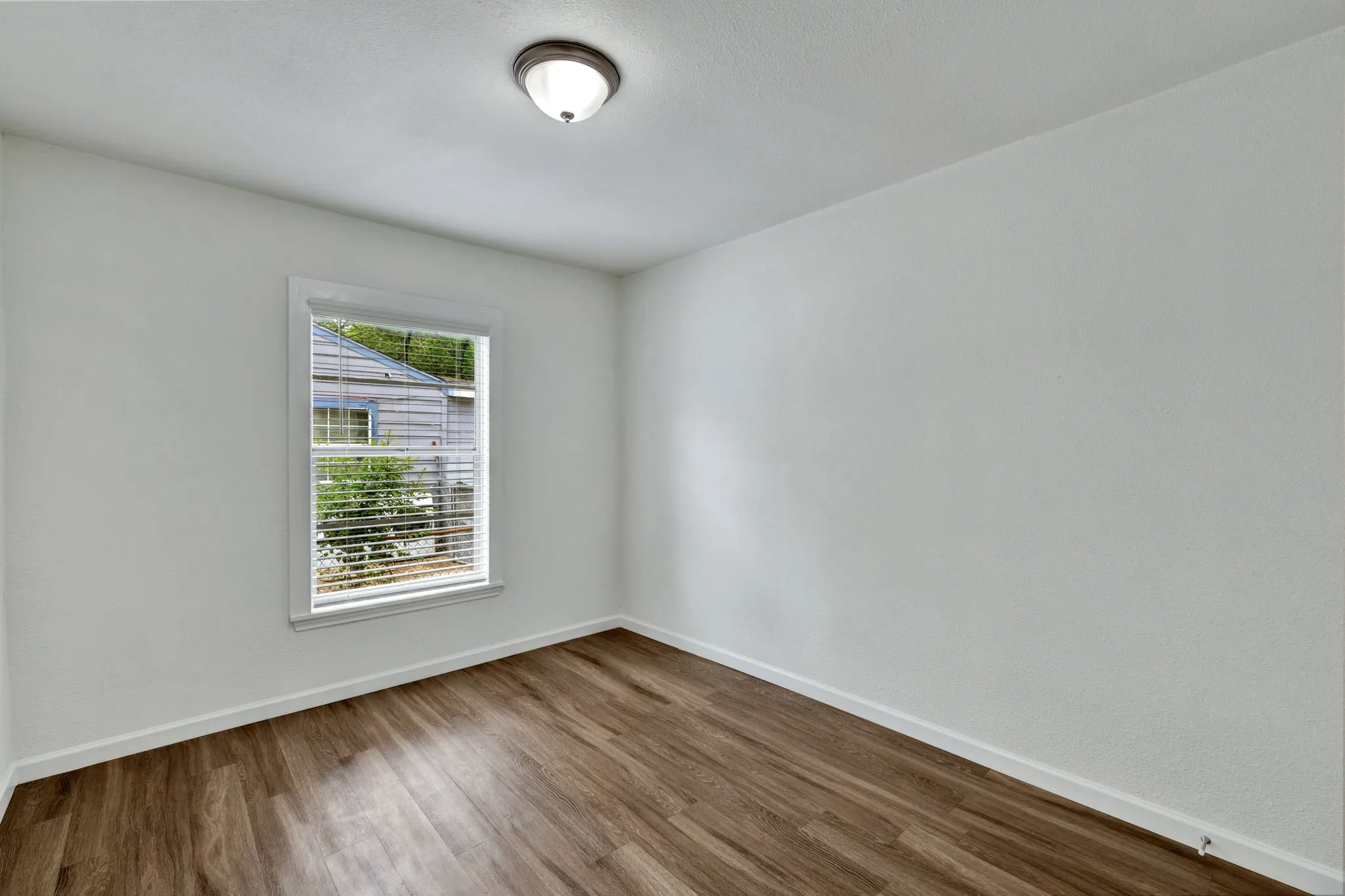 Interior room featuring wood-finish flooring, white painted walls, and a single window with blinds