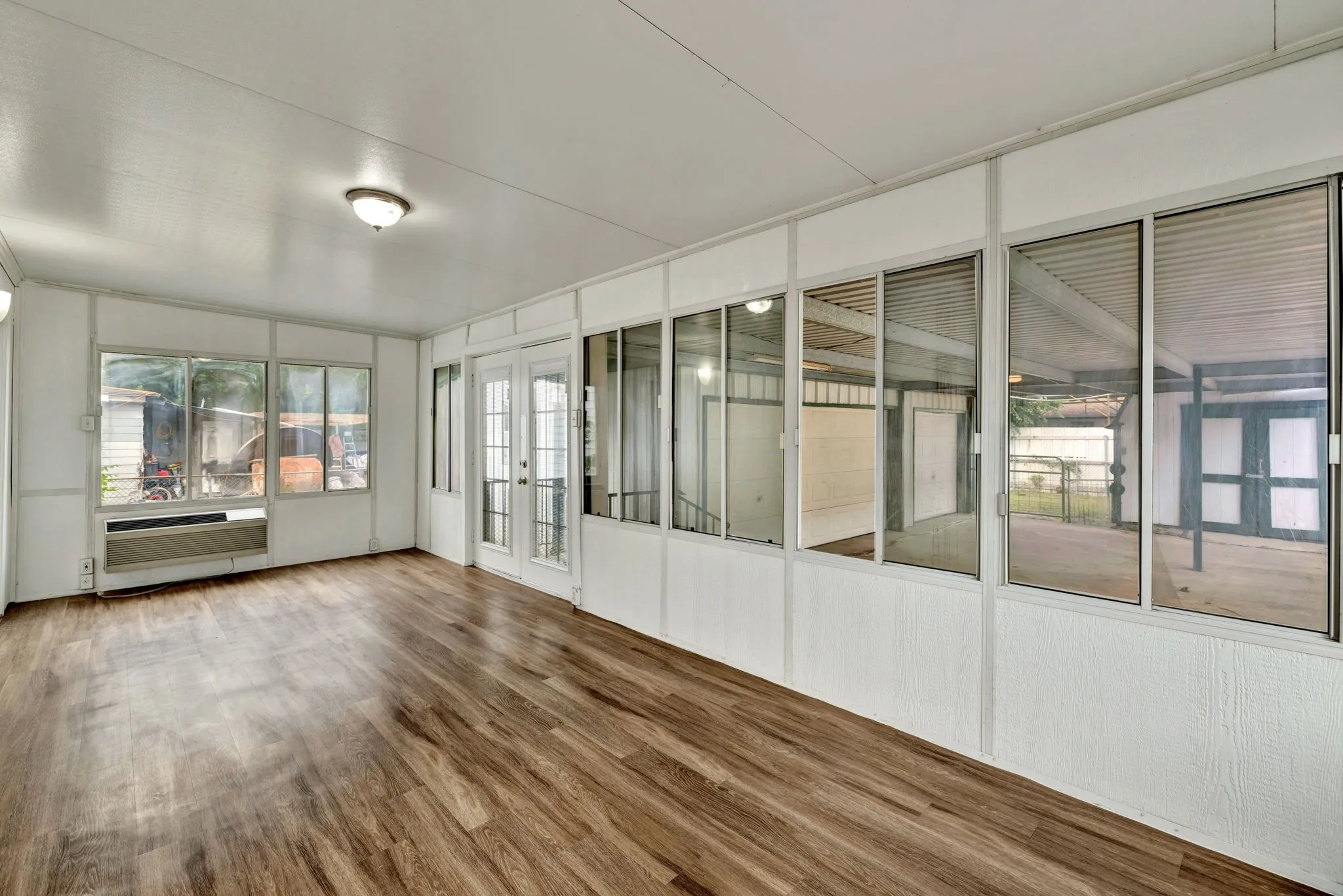 Enclosed sunroom featuring wood-finish flooring, white panel walls, multiple windows, and a double-door entry