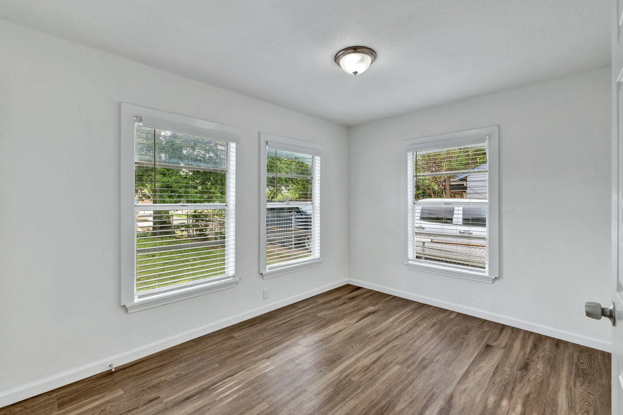 Room featuring wood-finish flooring, white walls, and three windows with blinds