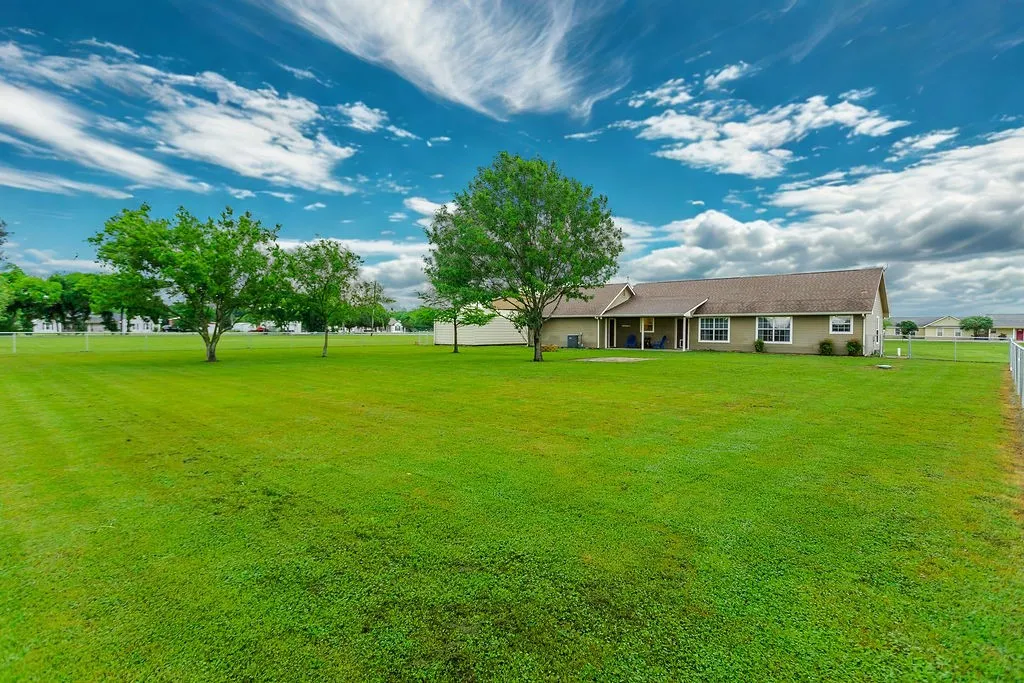 Expansive green lawn surrounding a single-story residence with a covered patio, multiple windows, and a partial chain-link fence