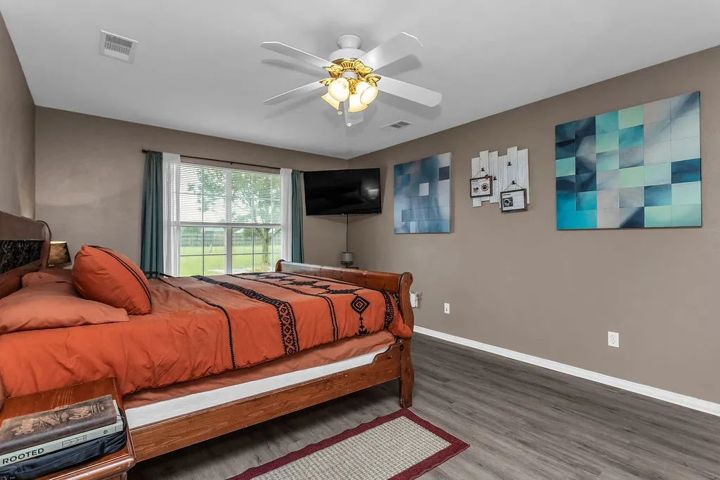 Bedroom featuring a window with exterior landscape, wood-finish flooring, a ceiling fan, and neutral wall tones
