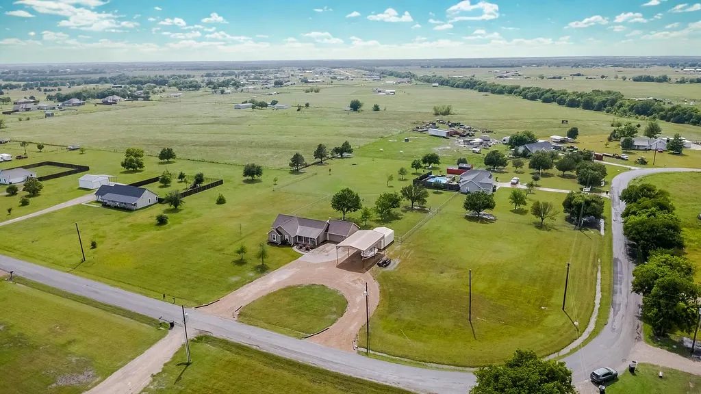 Expansive rural property featuring a primary residence with an attached carport, a separate outbuilding, and a circular gravel driveway