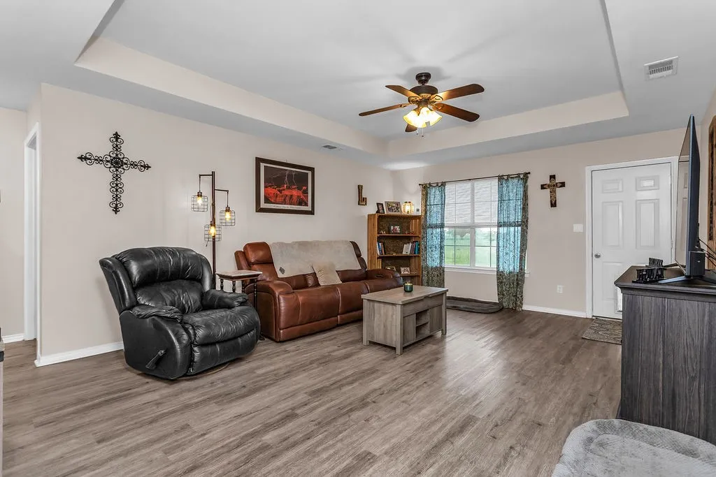 Spacious living area featuring wood-finish flooring, a tray ceiling, and a ceiling fan with integrated lighting