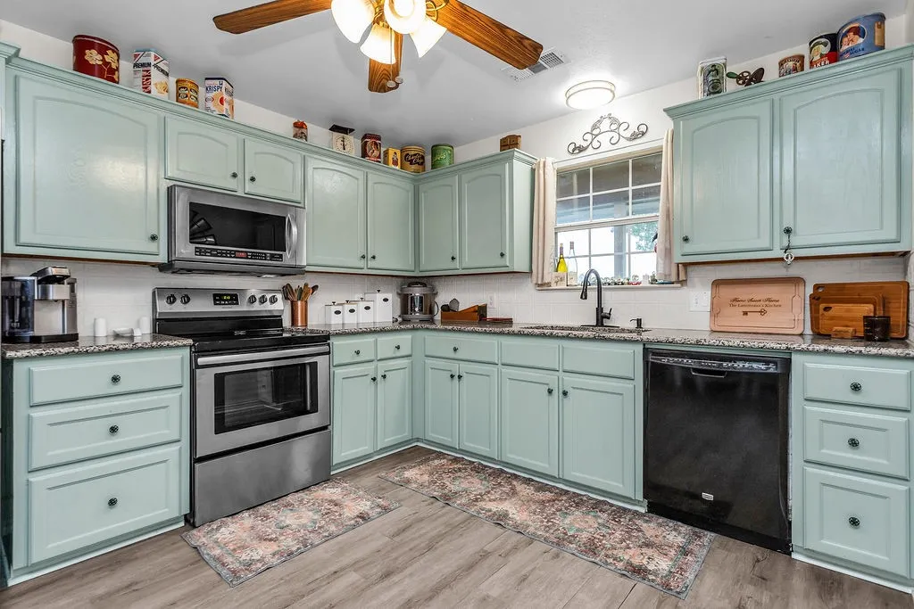Kitchen featuring light blue cabinetry, speckled countertops, stainless steel appliances, wood-finish flooring, and a ceiling fan