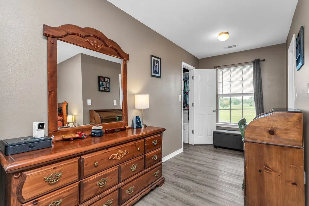Spacious room featuring wood-finish flooring, a bright window with horizontal blinds, a white paneled door revealing a closet, and neutral wall tones