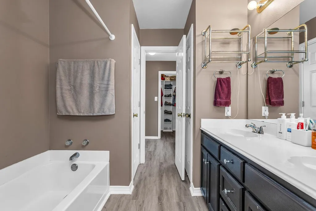 Bathroom featuring a white bathtub, a double vanity with dark cabinetry, and wood-finish flooring