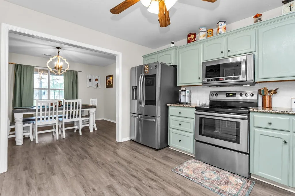 Kitchen featuring light green cabinetry, stainless steel appliances, speckled countertops, and wood-finish flooring