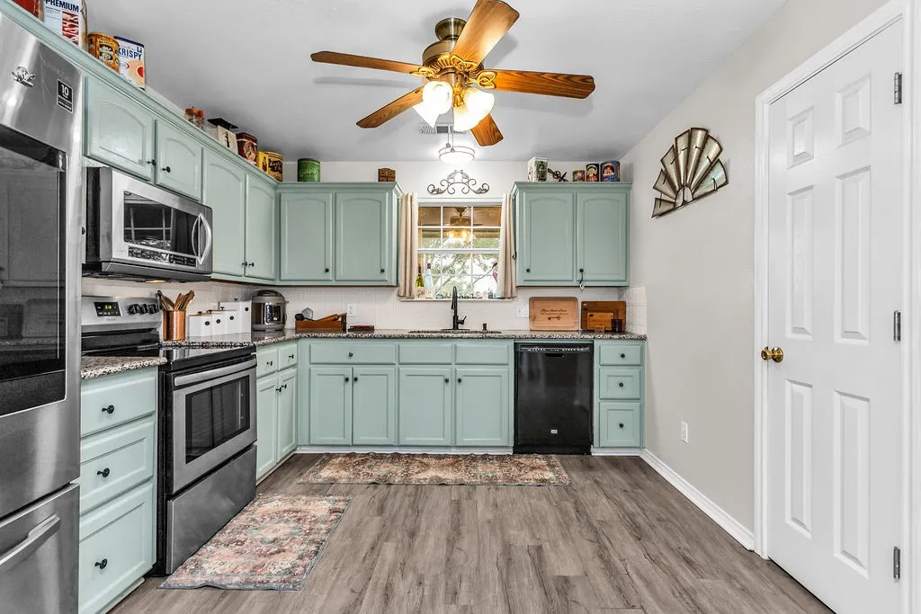 Kitchen featuring mint-colored cabinetry, stainless steel appliances, wood-finish flooring, a ceiling fan with integrated lighting, and a window above the sink
