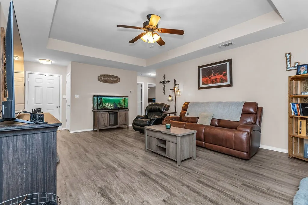 Spacious living area featuring wood-finish flooring, a tray ceiling, and a ceiling fan with integrated lighting