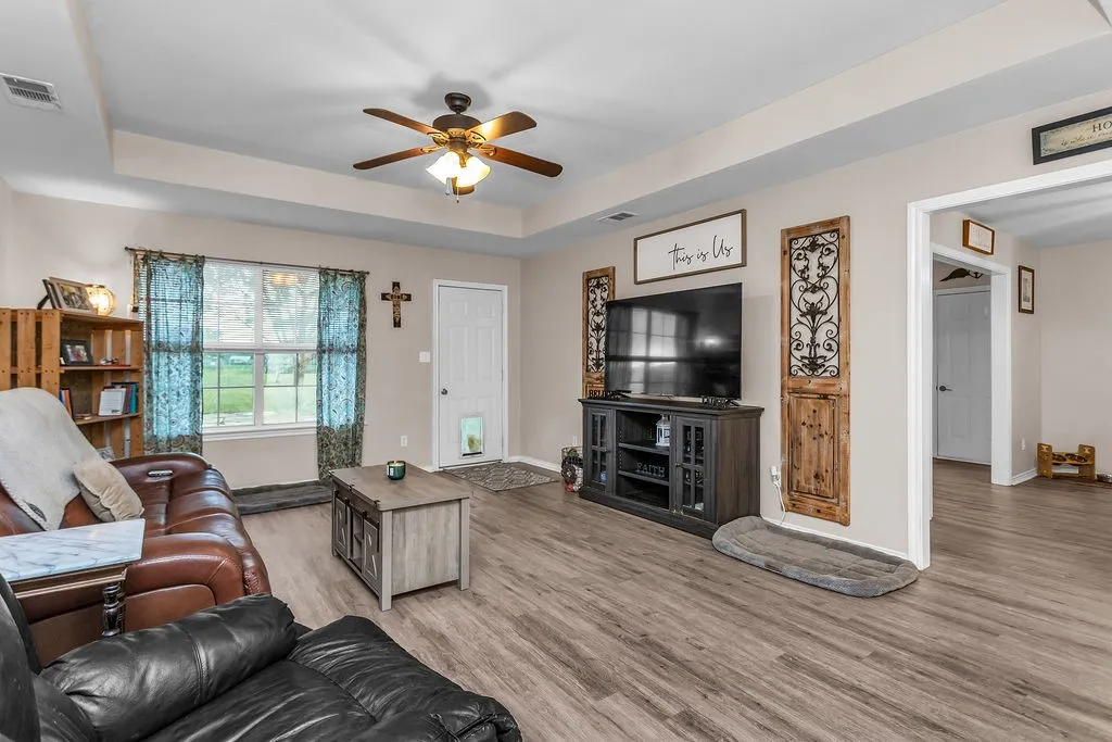Spacious living area featuring wood-finish flooring, a tray ceiling, and a ceiling fan