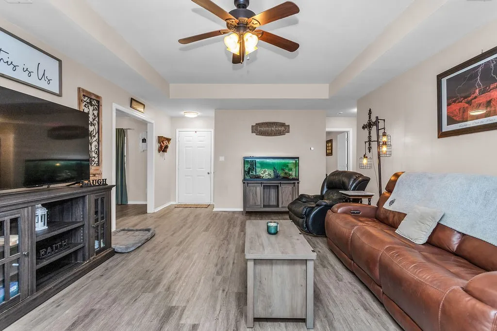 Spacious living area featuring wood-finish flooring, a tray ceiling with a ceiling fan, and recessed lighting
