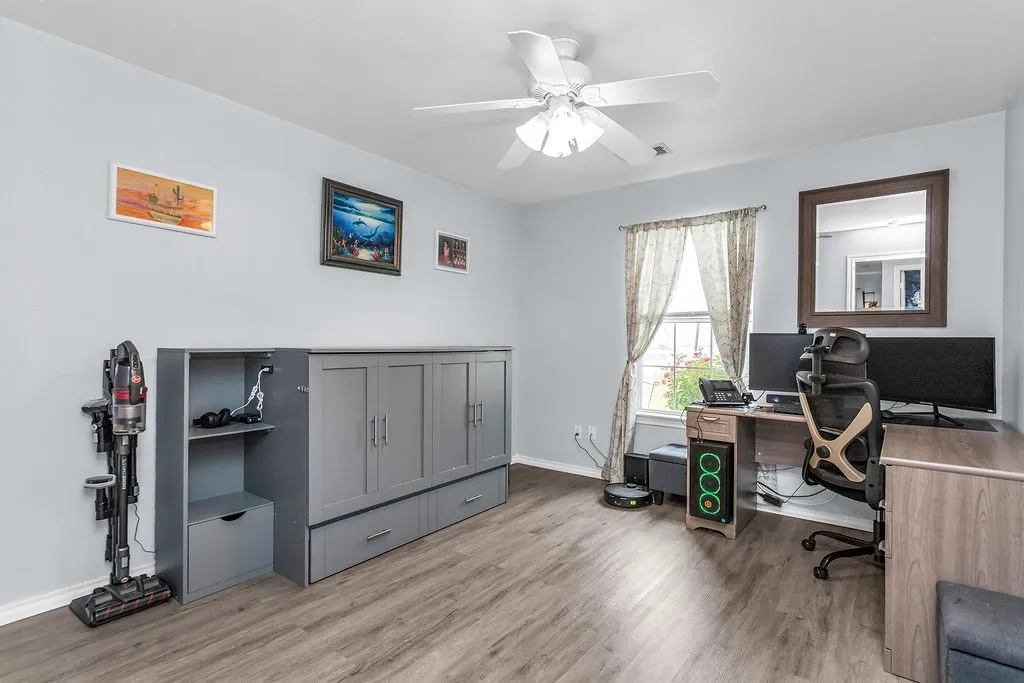Room featuring wood-finish flooring, a ceiling fan with light fixture, and a window with curtains