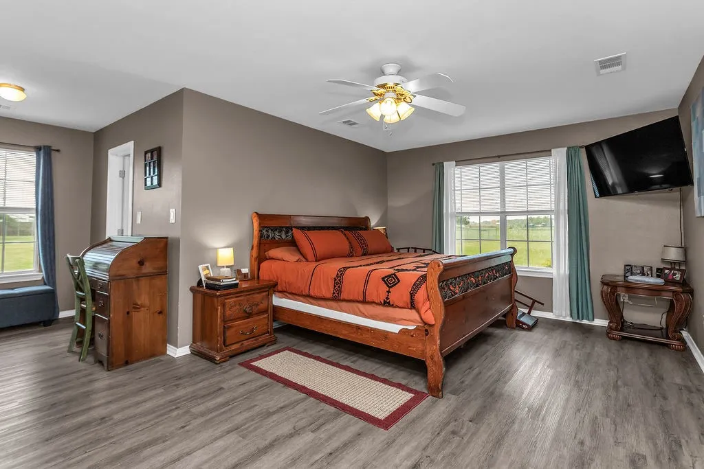 Spacious room featuring wood-finish flooring, two windows, and a ceiling fan