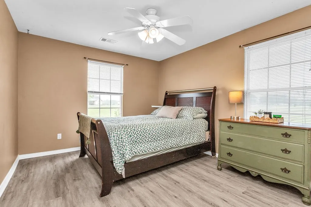 Bedroom featuring wood-finish flooring, two windows with blinds, a ceiling fan with integrated lighting, and neutral wall tones