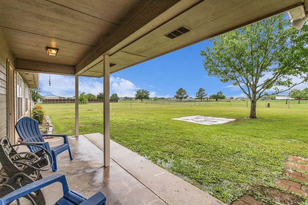 Covered back patio with concrete flooring, recessed lighting, and a large grassy area with mature trees