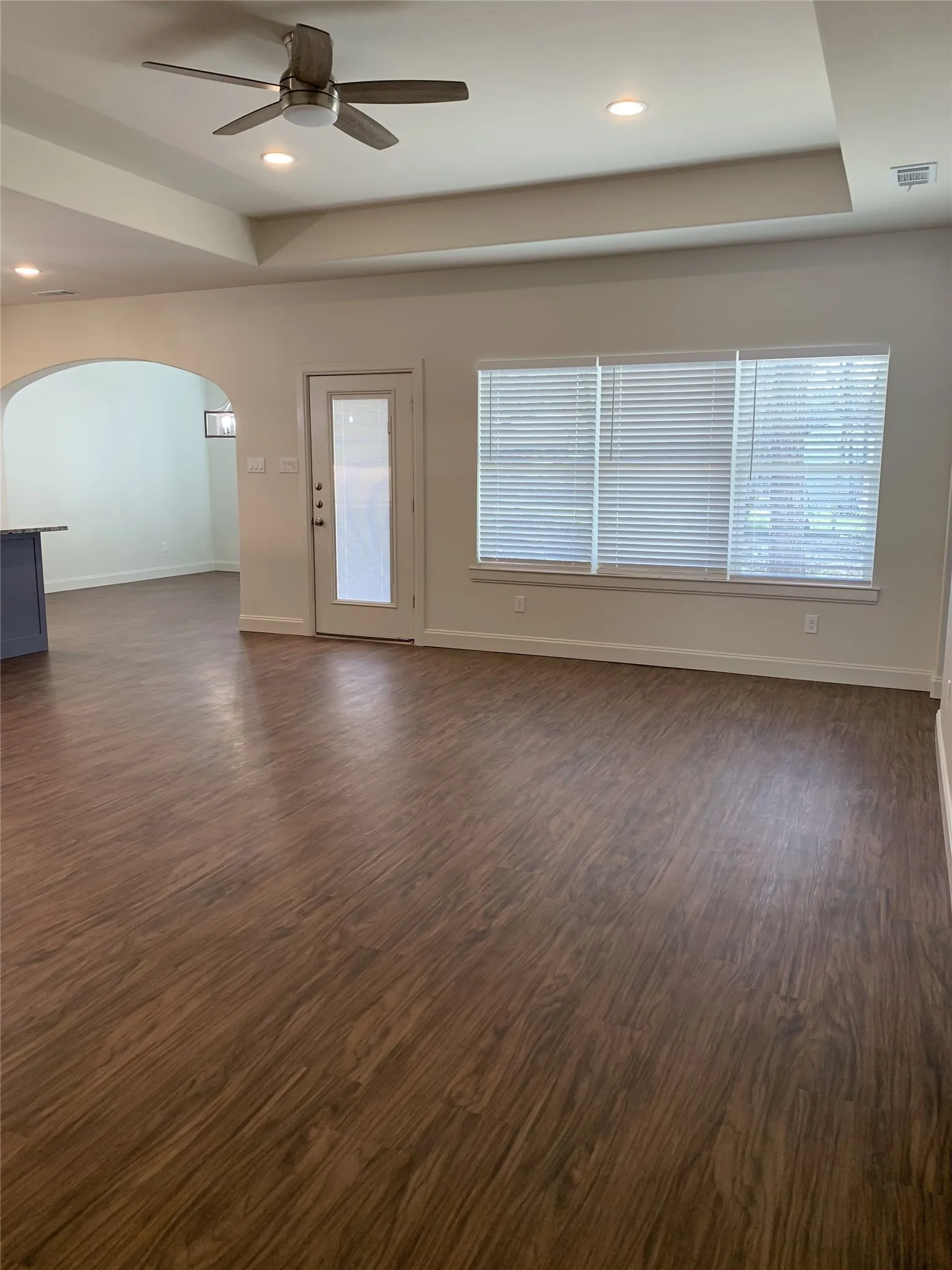 Expansive main living area featuring wood-finish flooring, a tray ceiling with recessed lighting, and a contemporary ceiling fan