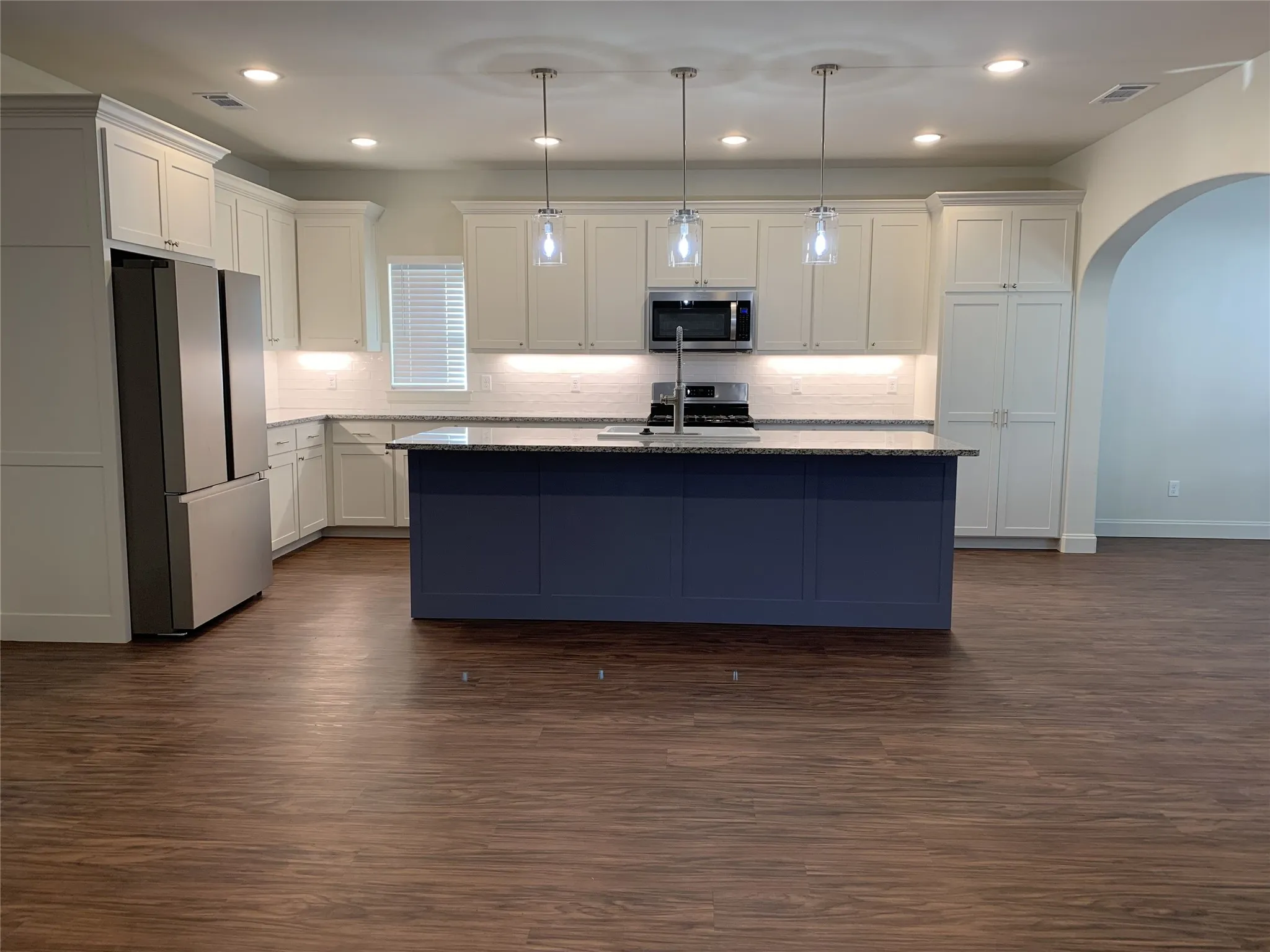 Kitchen featuring a deep blue island with a stone countertop, white shaker cabinetry, stainless steel appliances, and wood-finish flooring